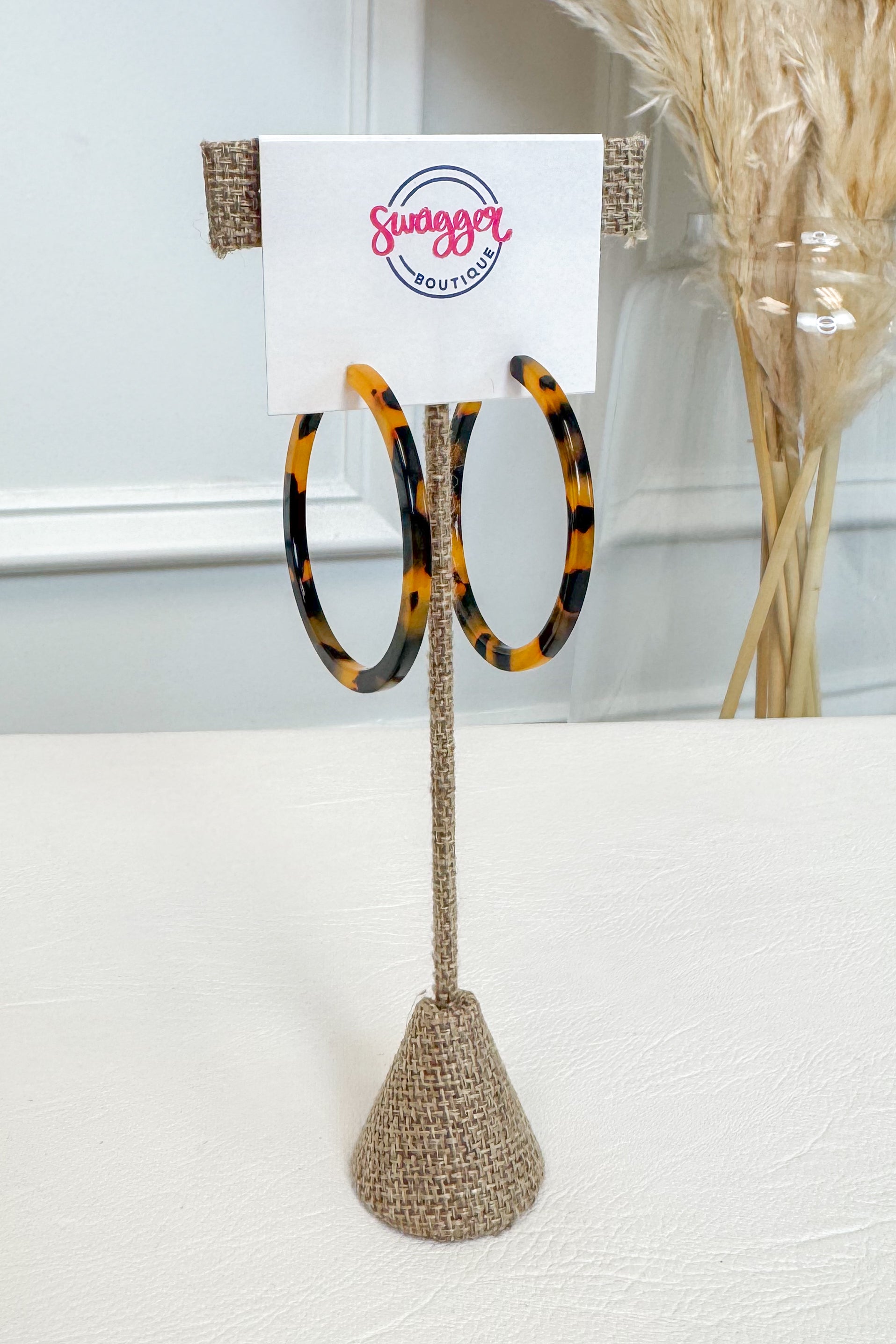 Tortoiseshell hoop earrings displayed on a burlap-covered stand with a white card labeled &