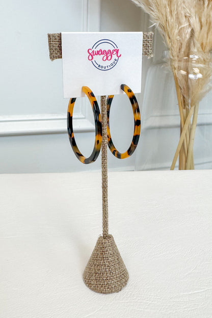 Tortoiseshell hoop earrings displayed on a burlap-covered stand with a white card labeled &