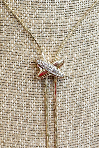 Close up of Gold-tone delicate chain necklace featuring a elongated vertical X pendant on a beige jewelry bust
