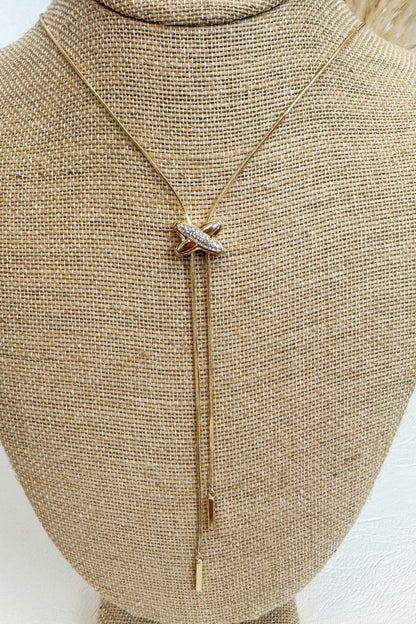  Gold-tone delicate necklace featuring a elongated vertical X pendant on a beige jewelry bust