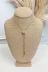 Gold-tone delicate chain necklace featuring a small elongated vertical X pendant on a beige jewelry bust