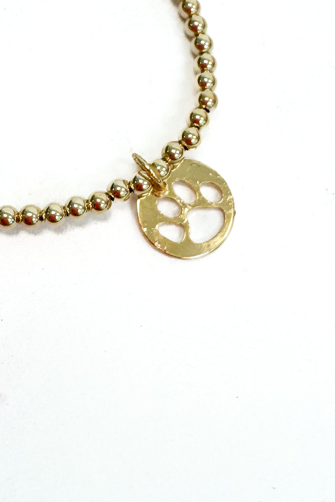 Gold beaded bracelet with a paw print charm on a white background