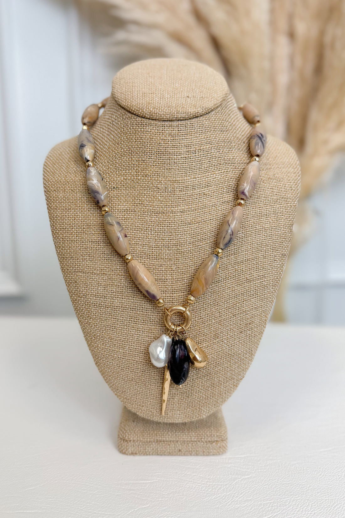 front view of tan necklace with pearl, plum, and gold accent charms on bust