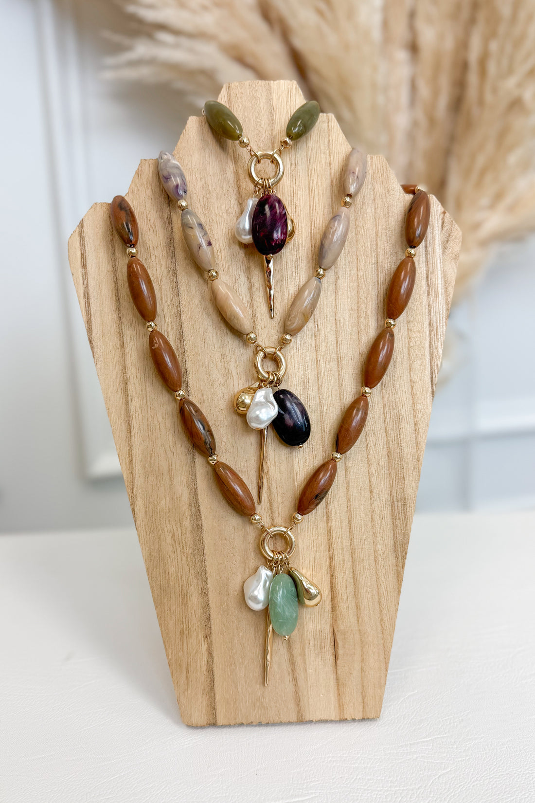 front view of all three marble stone multi charm necklaces necklaces with pearl, plum, sea-foam, and gold accent charms on wooden bust 