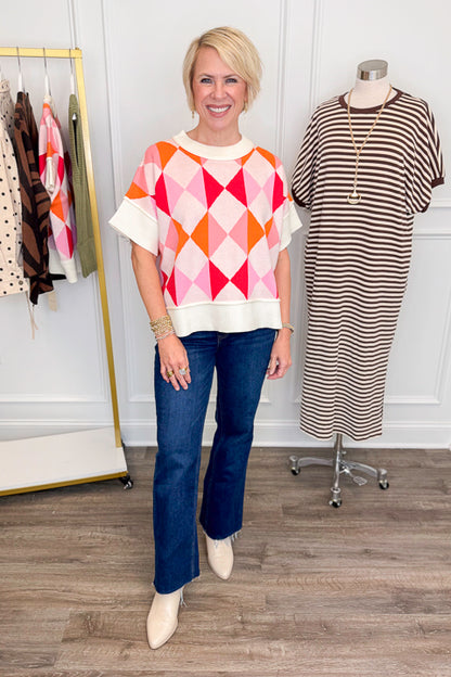 Front view of woman wearing Swagger Boutique’s Pink Color Block Short Sleeve Sweater with jeans with clothing hanging in the background.