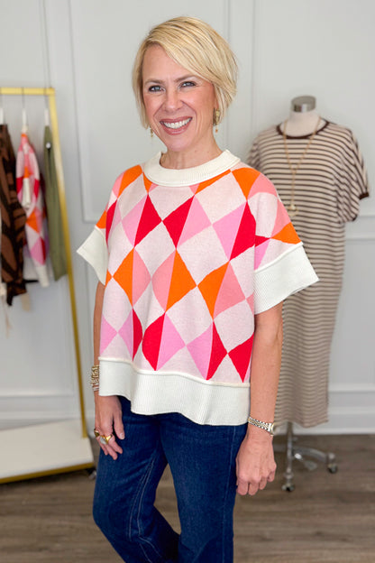 Side view of woman wearing Swagger Boutique’s Pink Color Block Short Sleeve Sweater with jeans with clothing hanging in the background.