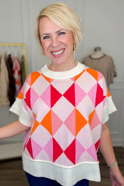 Front view of woman wearing Swagger Boutique’s Pink Color Block Short Sleeve Sweater with jeans with clothing hanging in the background.