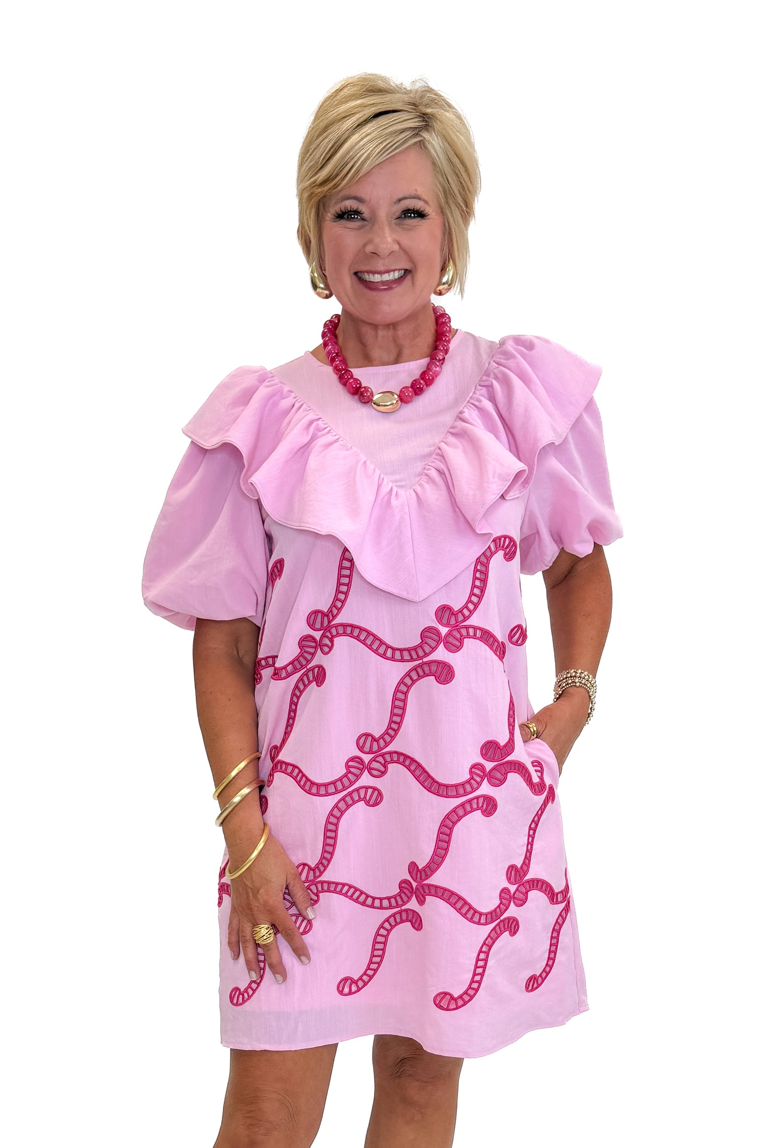Front view of woman wearing Swagger Boutique’s Pink Embroidered Ruffle Mini Dress with heels against white studio background.