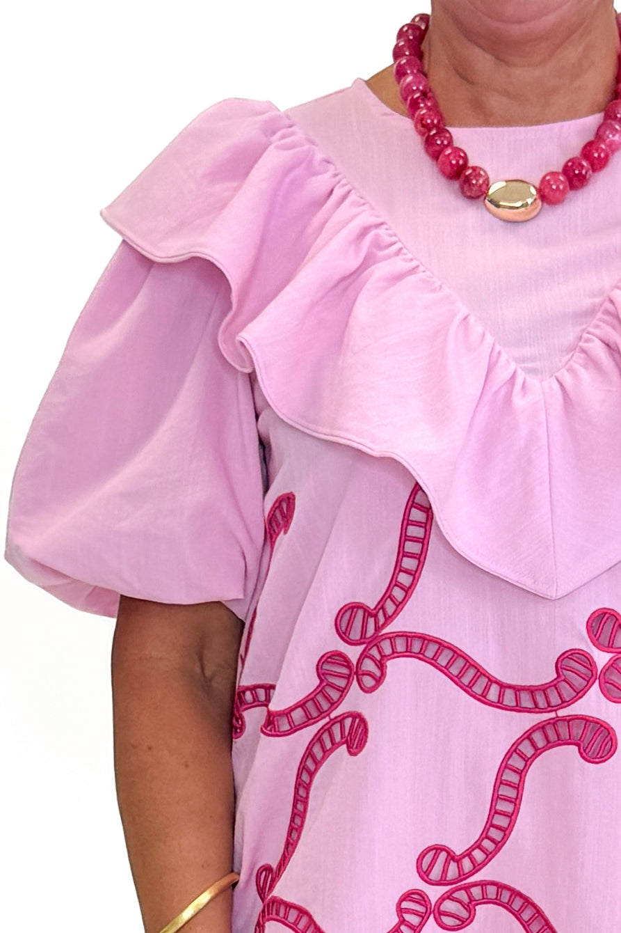 Front detail view of woman wearing Swagger Boutique’s Pink Embroidered Ruffle Mini Dress with heels against white studio background.