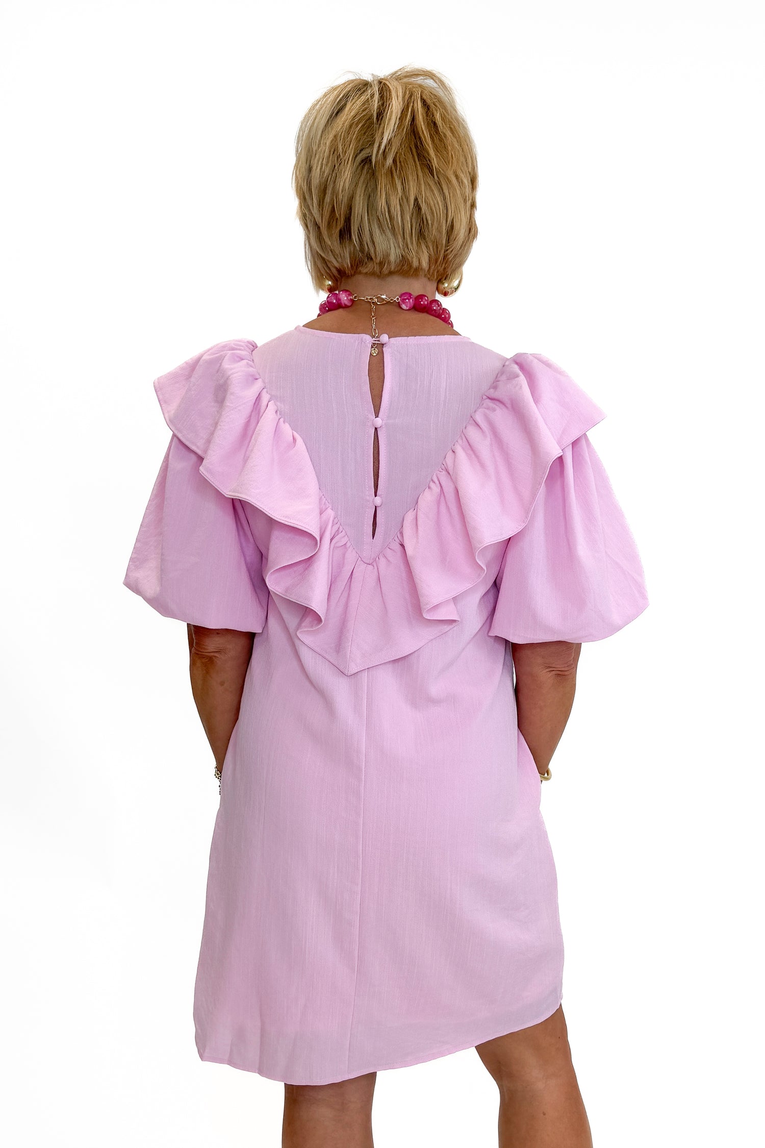 Back view of woman wearing Swagger Boutique’s Pink Embroidered Ruffle Mini Dress with heels against white studio background.