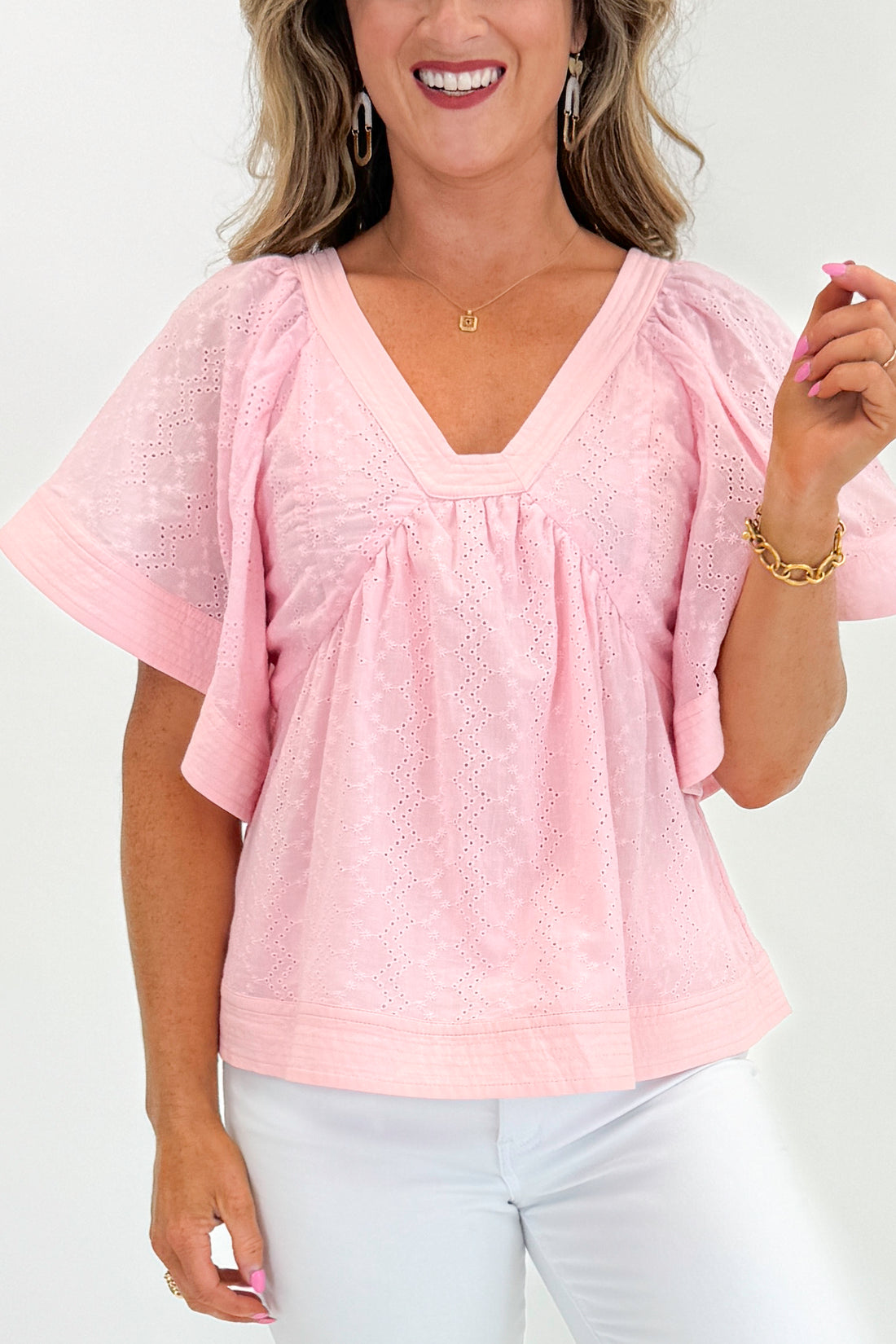 Front view of woman wearing Swagger Boutique’s Pink Eyelet V-Neck Top with jeans against white studio background.