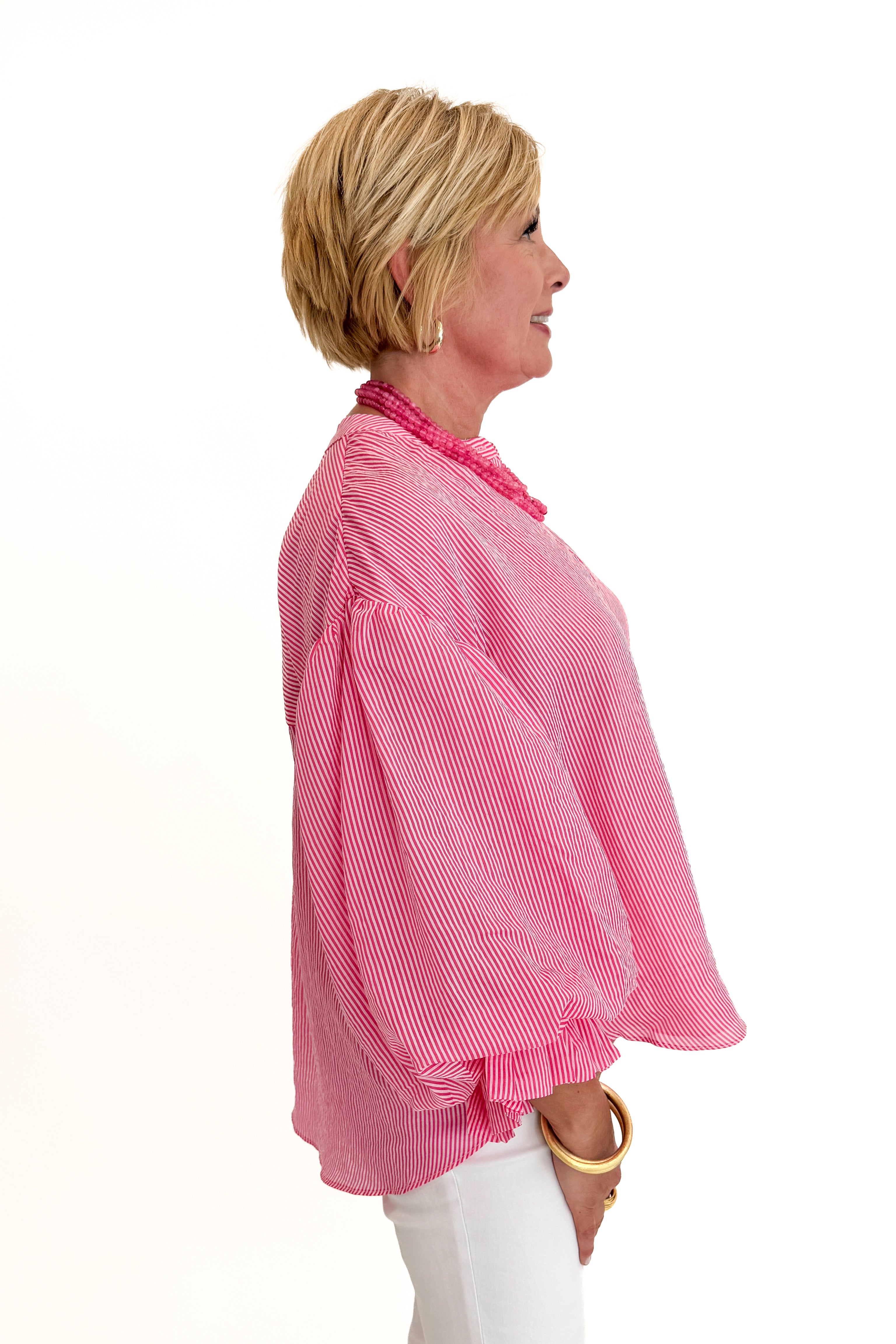 Side view of woman wearing Swagger Boutique’s Pink Pinstripe Bubble Sleeve Top with jeans against white studio background.
