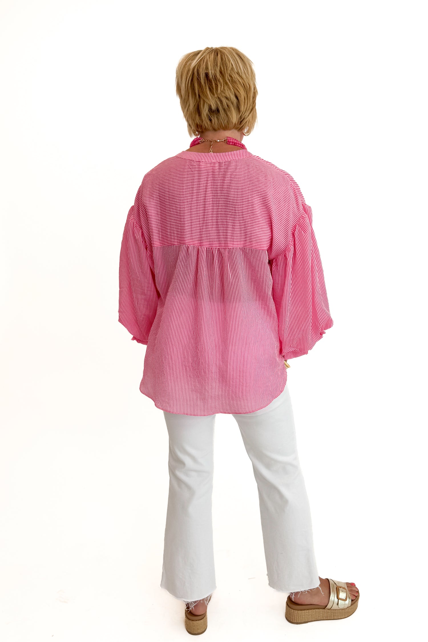 Back view of woman wearing Swagger Boutique’s Pink Pinstripe Bubble Sleeve Top with jeans against white studio background.