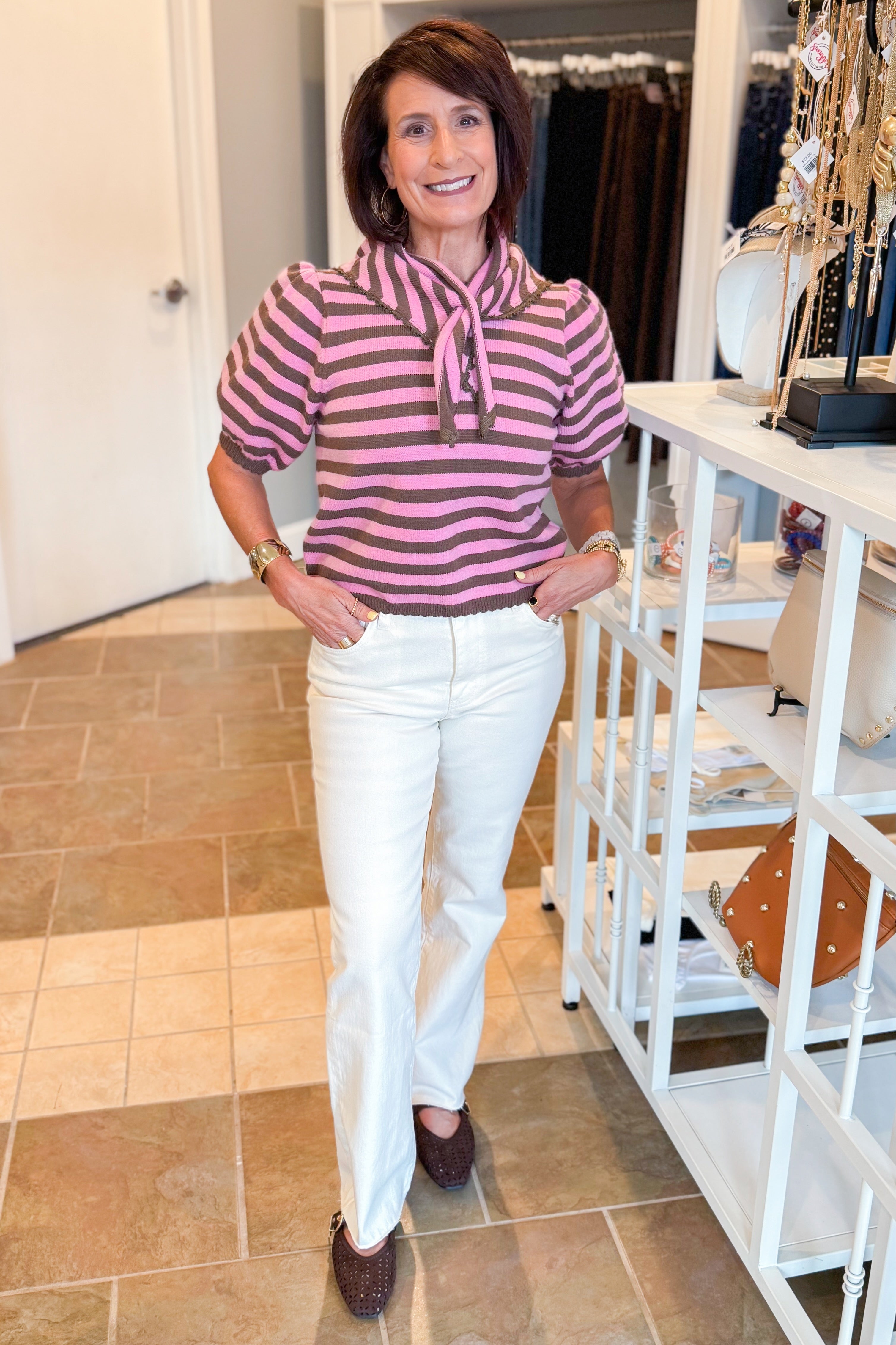 Front view of woman wearing Swagger Boutique’s Pink &amp; Brown Striped Faux Tie Short Sleeve Sweater by Entro with jeans standing at the store.