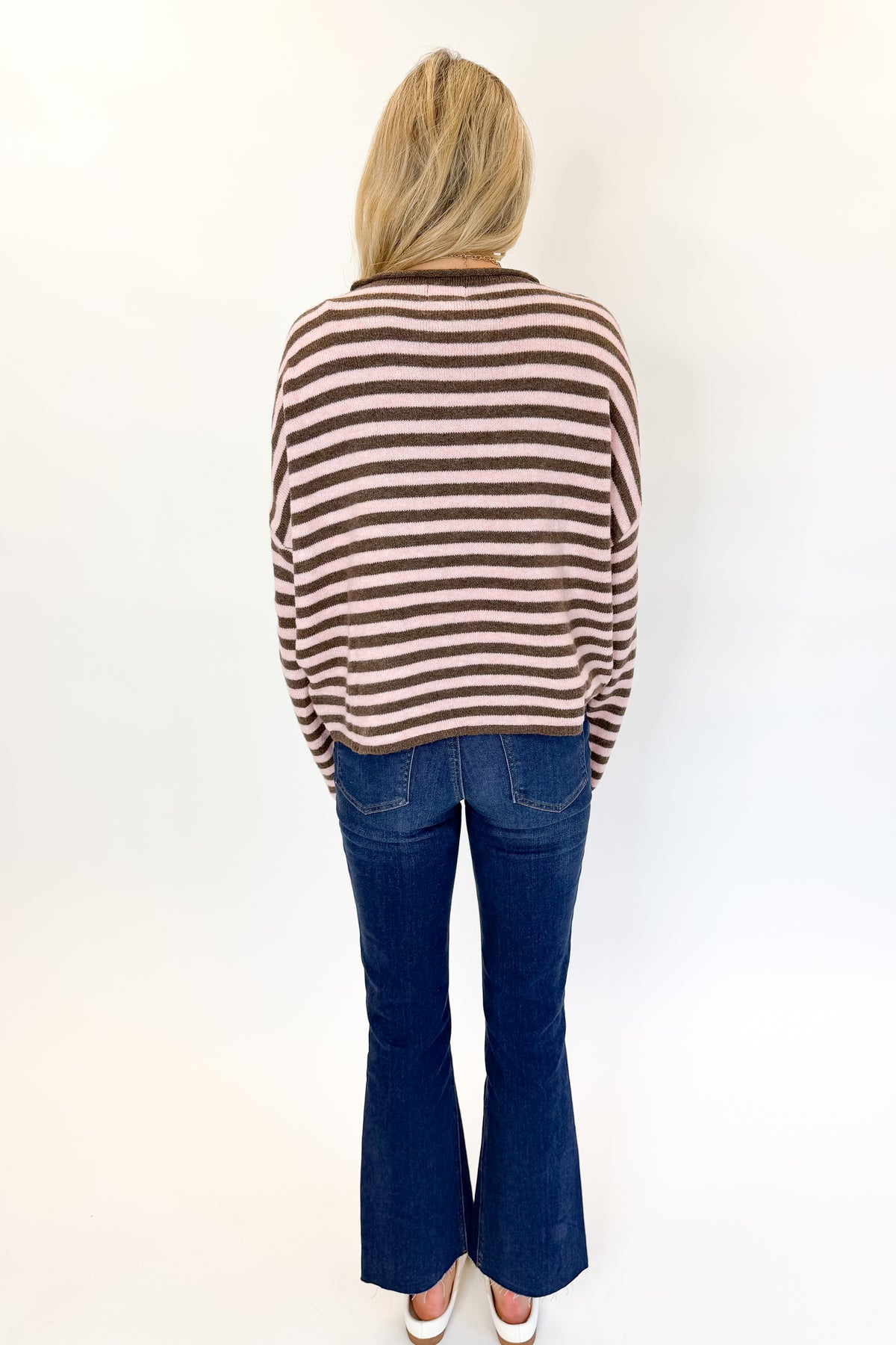 Back view of woman wearing Swagger Boutique’s Pink &amp; Brown Striped Sweater with jeans against white studio background.