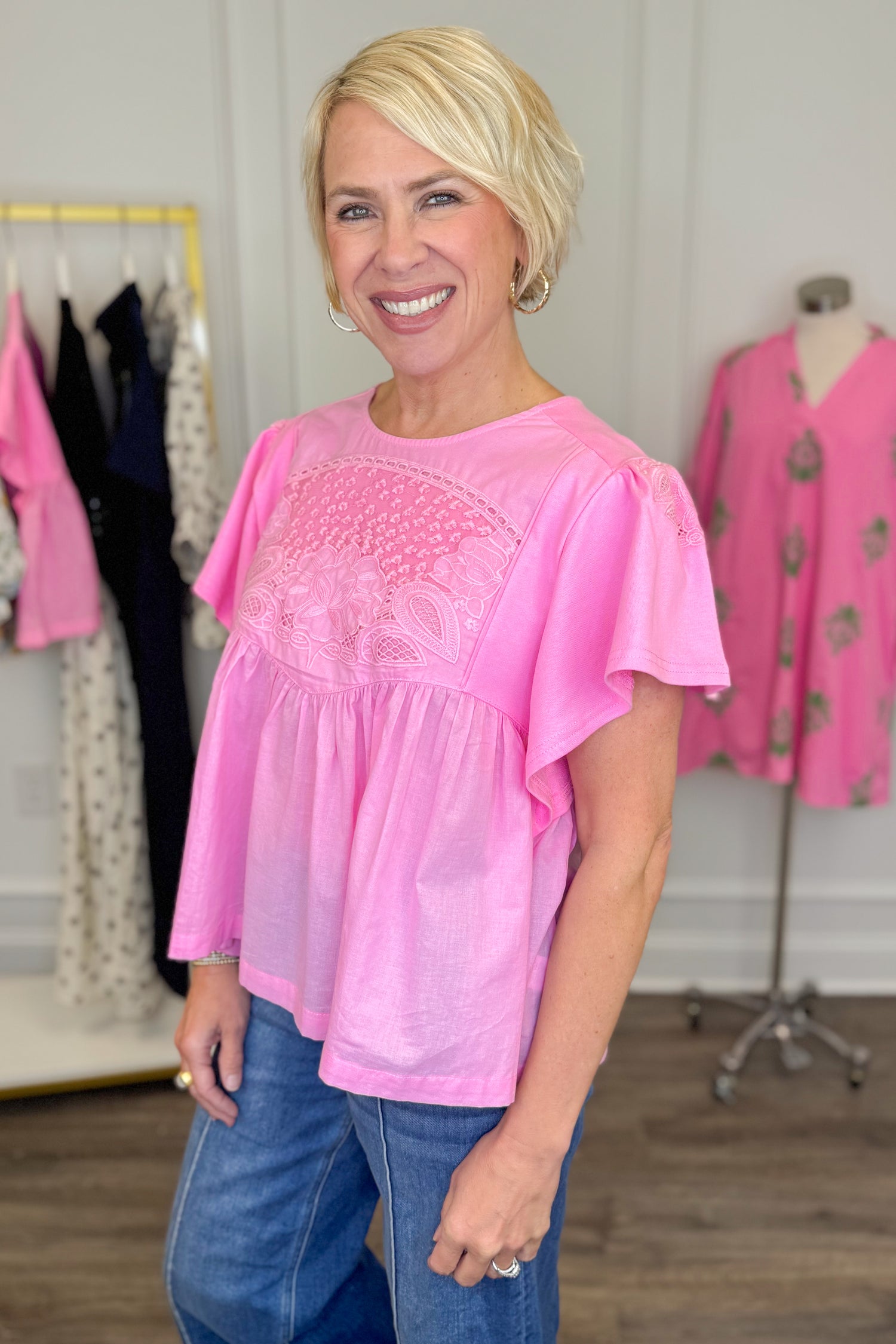 Side view of woman wearing Swagger Boutique’s Pink Embroidered Peplum Top with jeans with clothes around her.