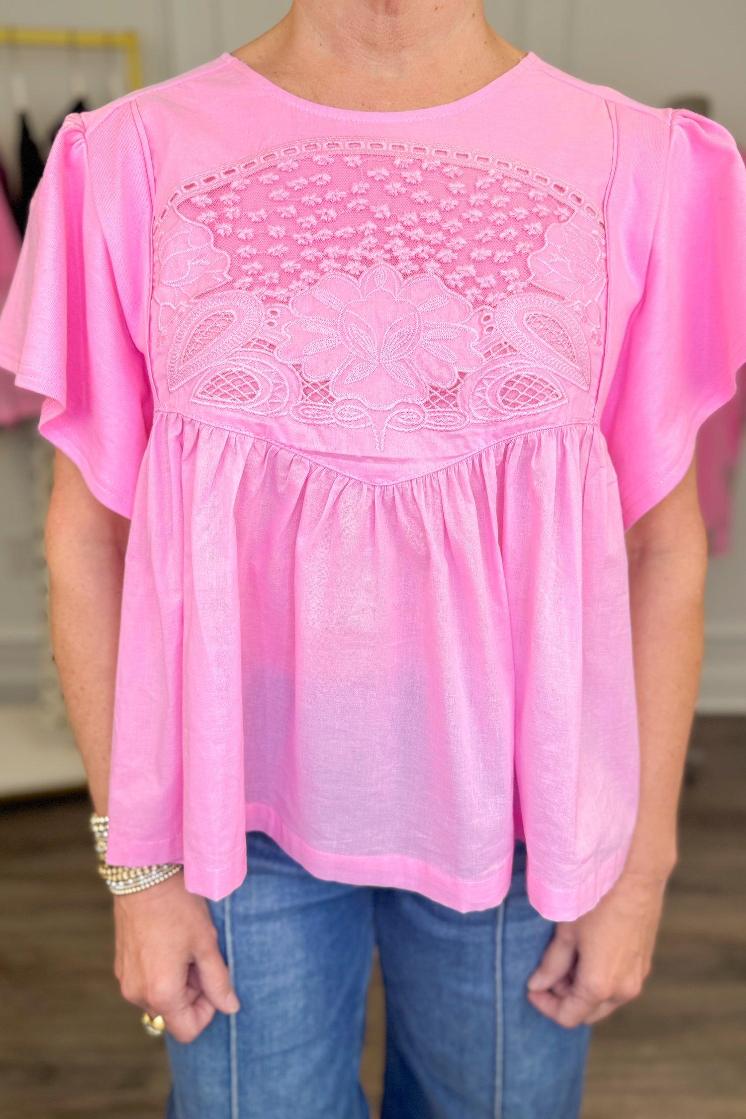 Front detail view of woman wearing Swagger Boutique’s Pink Embroidered Peplum Top with jeans with clothes around her.