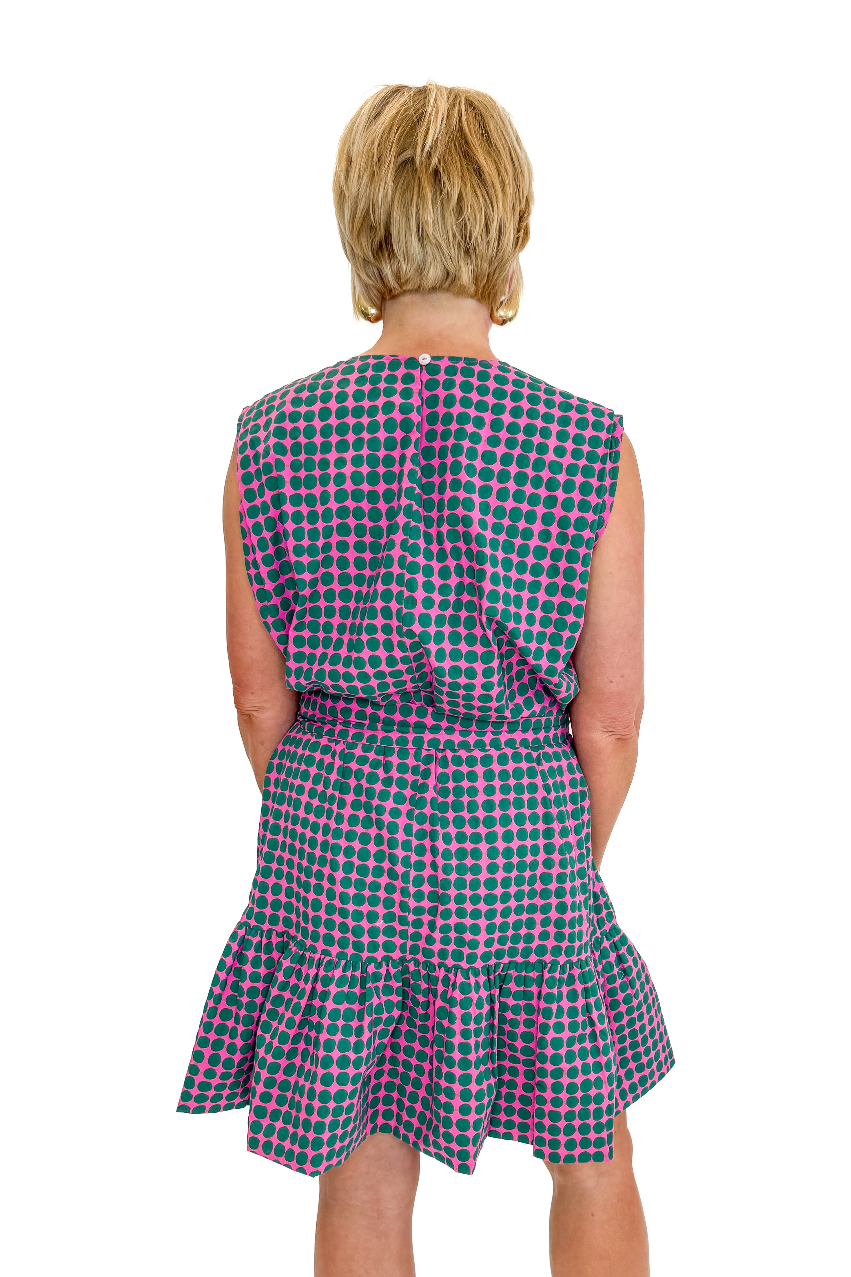 Back view of woman wearing Swagger Boutique’s Pink &amp; Green Polka Dot Mini Dress with sandals against white studio background.