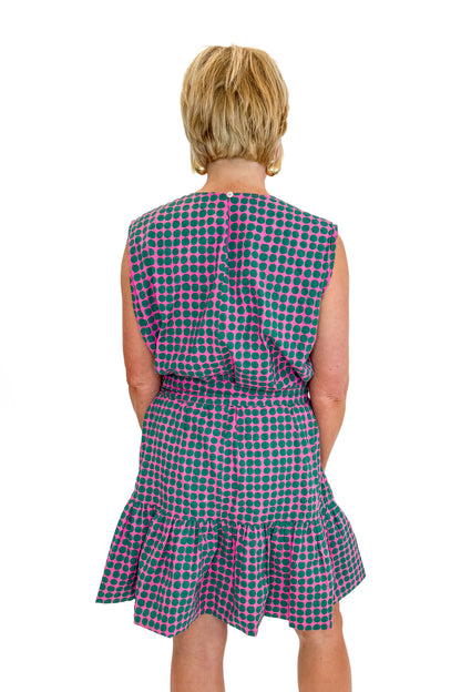 Back view of woman wearing Swagger Boutique’s Pink &amp; Green Polka Dot Mini Dress with sandals against white studio background.