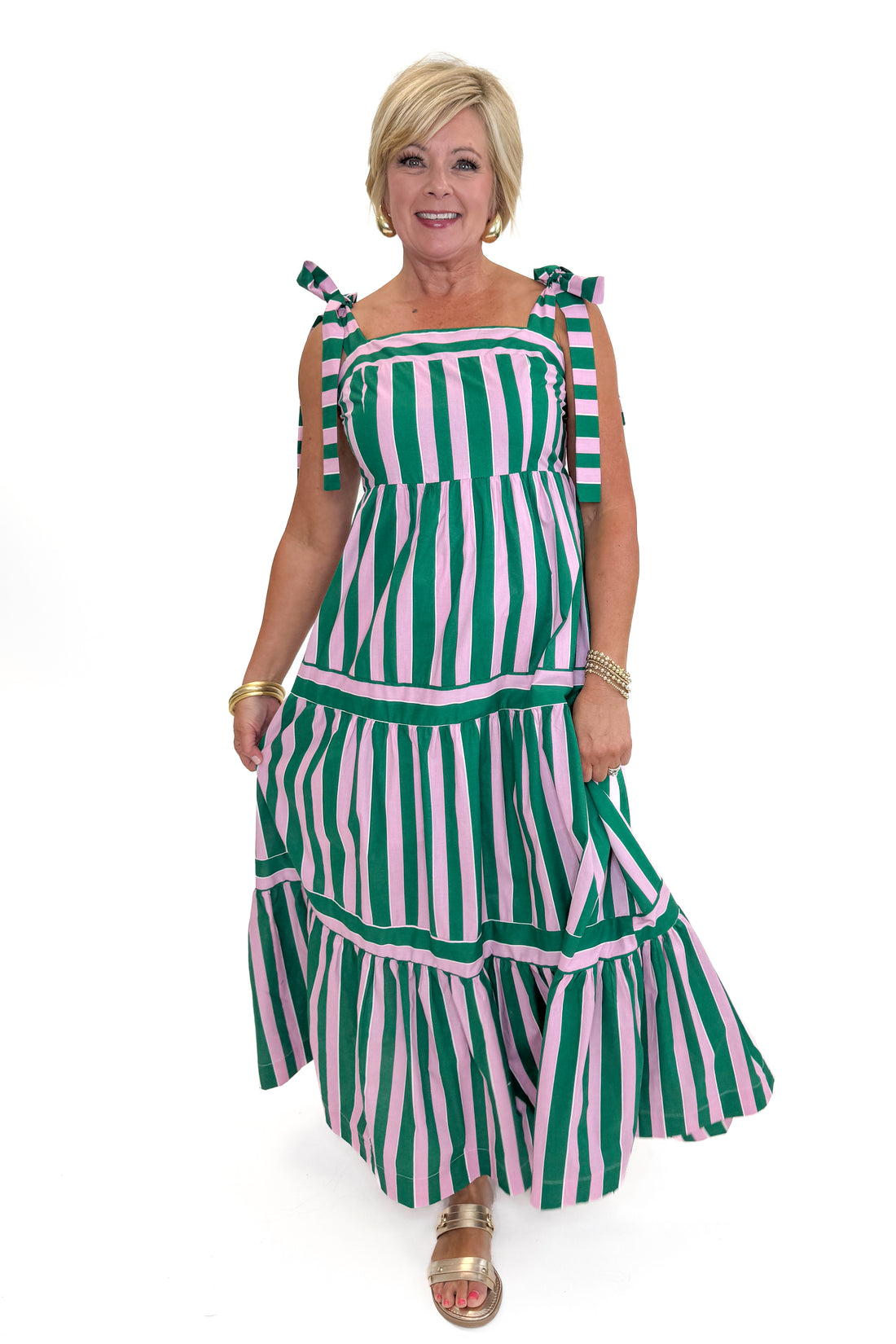 Front view of woman wearing Swagger Boutique’s Pink &amp; Green Striped Tiered Maxi Dress with sandals against white studio background.
