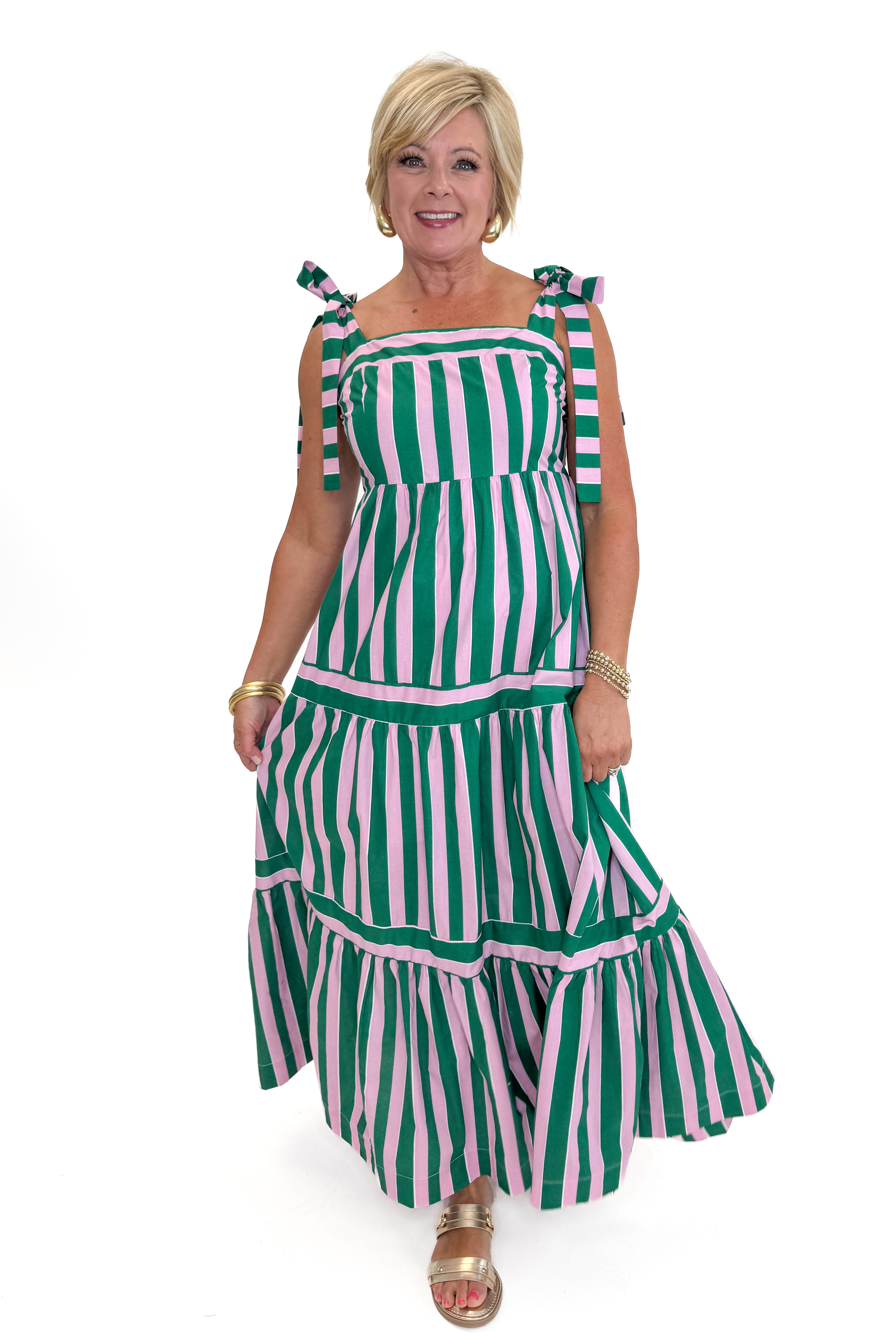 Front view of woman wearing Swagger Boutique’s Pink &amp; Green Striped Tiered Maxi Dress with sandals against white studio background.