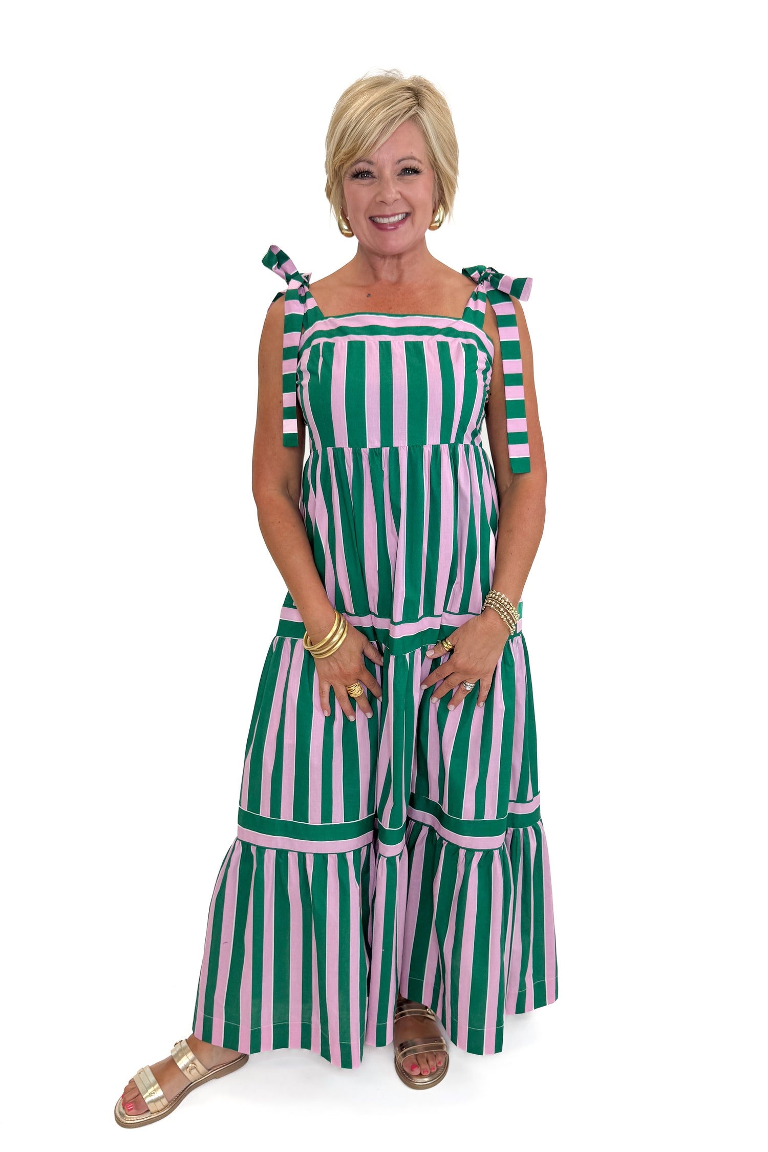 Front view of woman wearing Swagger Boutique’s Pink &amp; Green Striped Tiered Maxi Dress with sandals against white studio background.