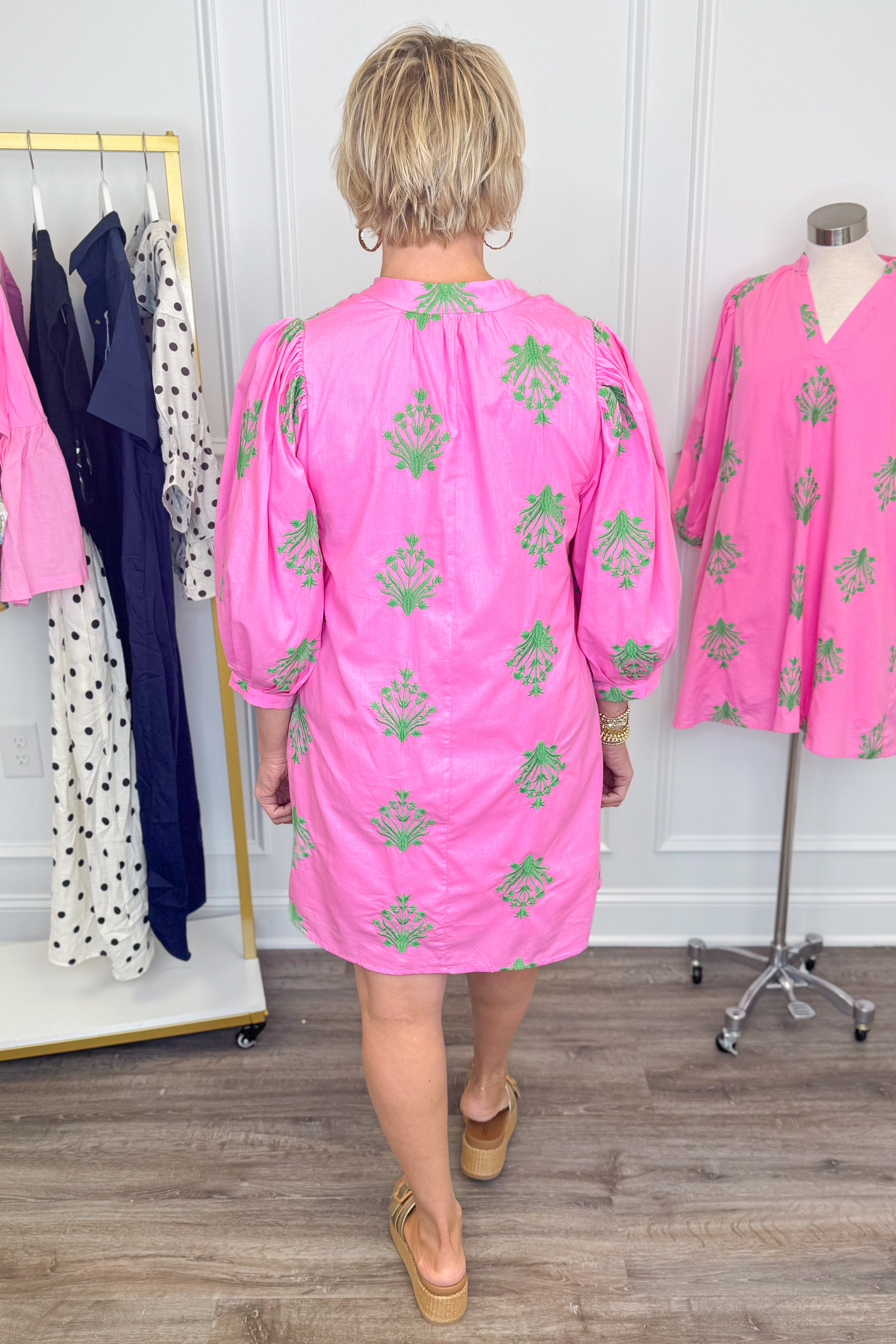 Back view of woman wearing Swagger Boutique’s Pink &amp; Green 3/4 Sleeve Embroidered Dress with sandals with clothes around her.