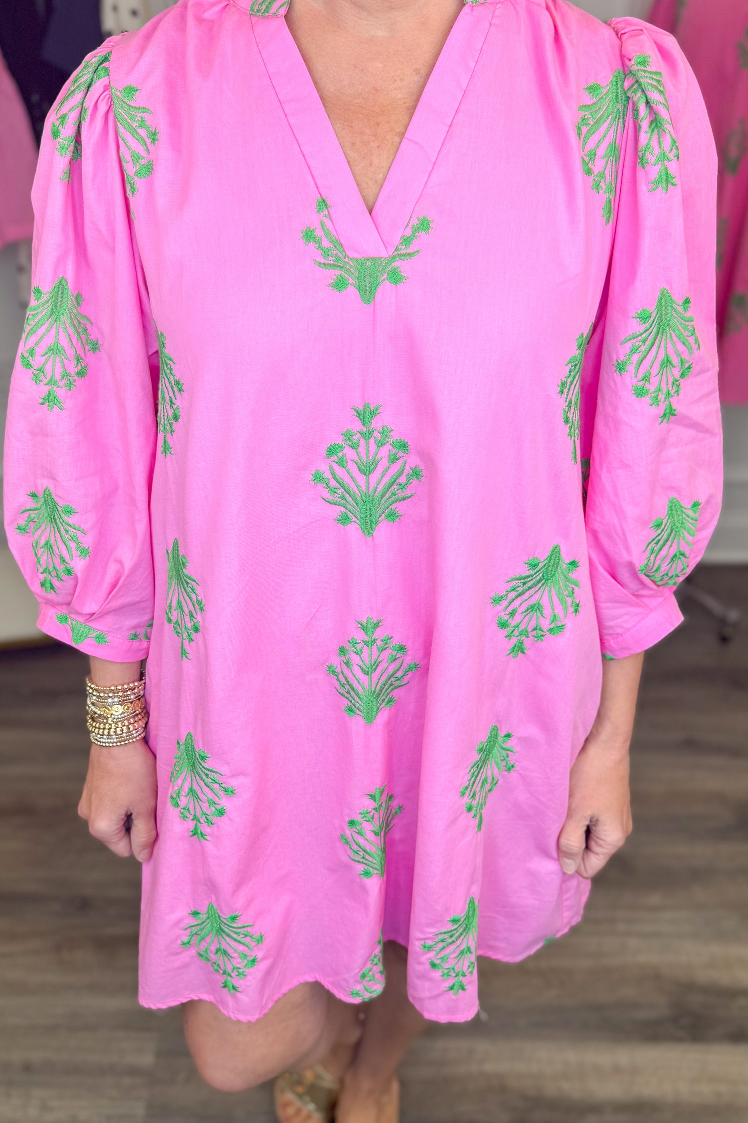 Front detail view of woman wearing Swagger Boutique’s Pink &amp; Green 3/4 Sleeve Embroidered Dress with sandals with clothes around her.