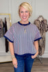 Front view of woman wearing Swagger Boutique’s Pink & Green Striped Short Sleeve Sweater with jeans with clothing hanging in the background.