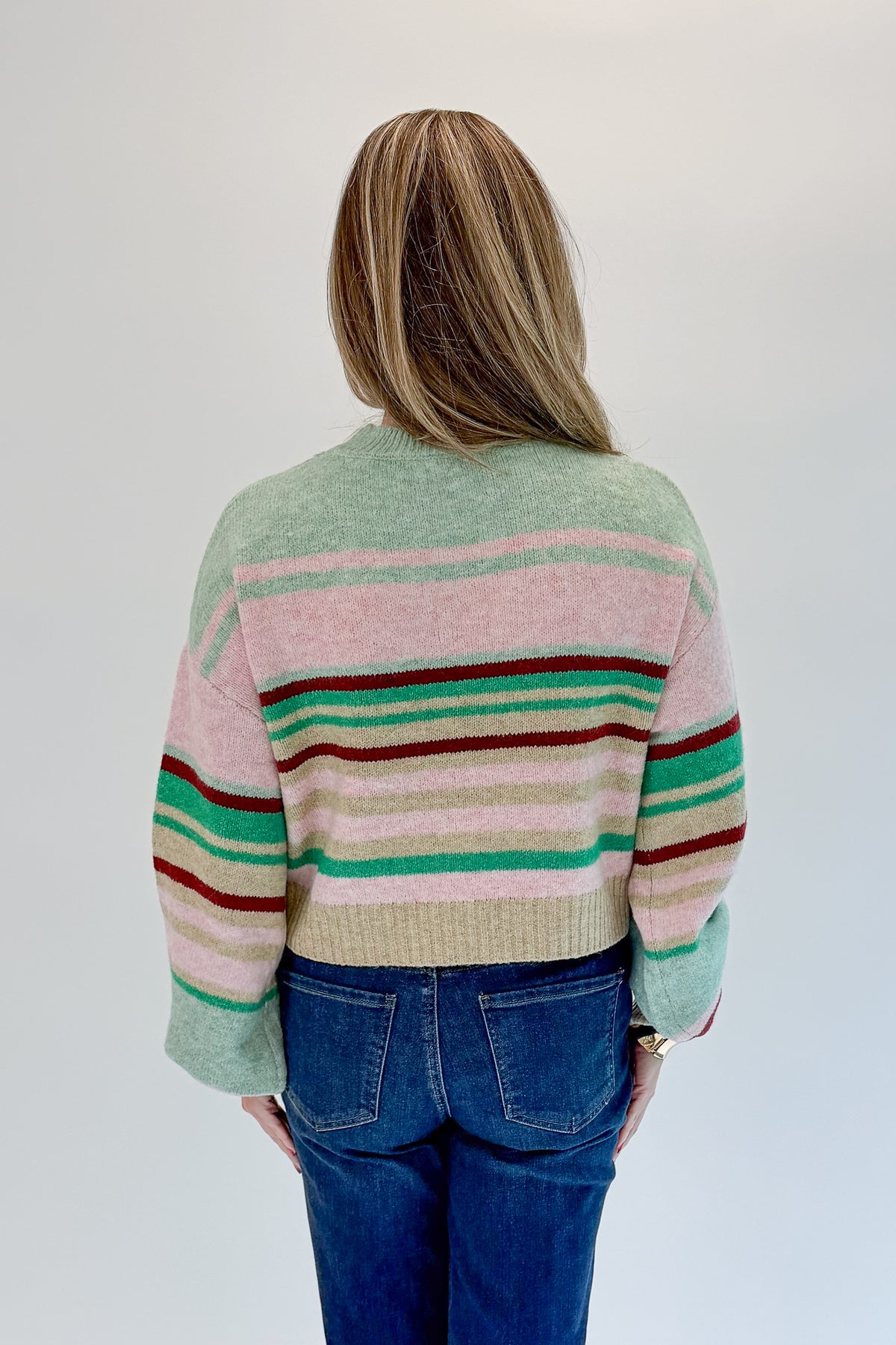 Back view of woman wearing Swagger Boutique’s Pink &amp; Multi Striped Sweater with jeans against white studio background.