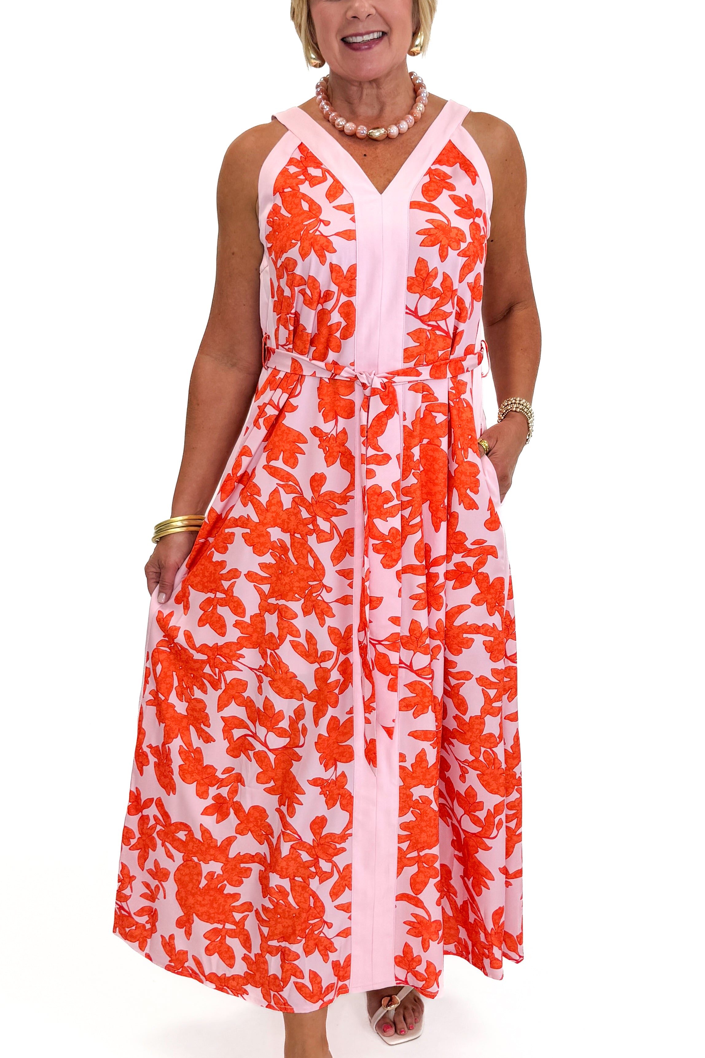 Front detail view of woman wearing Swagger Boutique’s Pink &amp; Orange Floral Midi Dress by Entro with heels against white studio background.