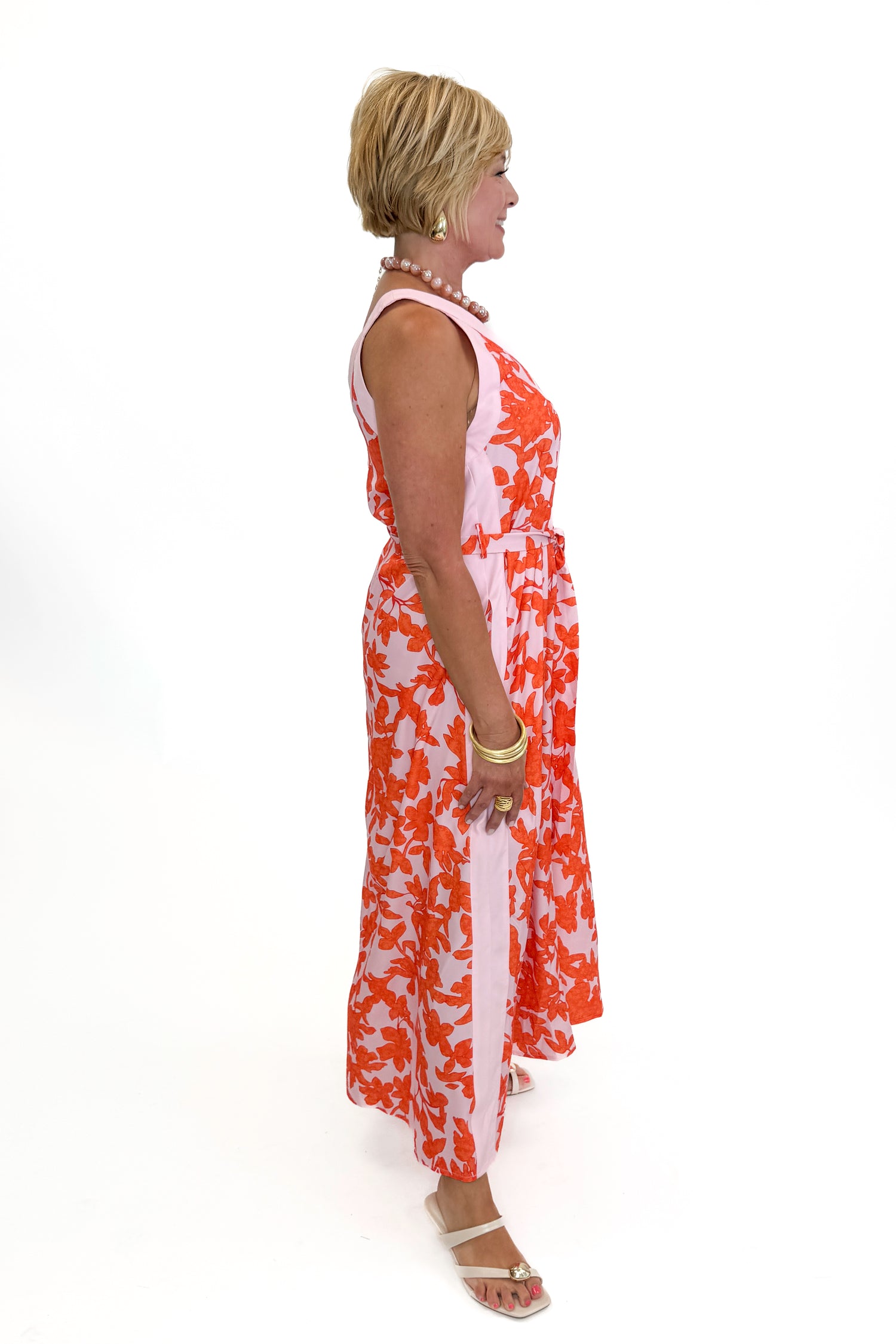 Side view of woman wearing Swagger Boutique’s Pink &amp; Orange Floral Midi Dress by Entro with heels against white studio background.