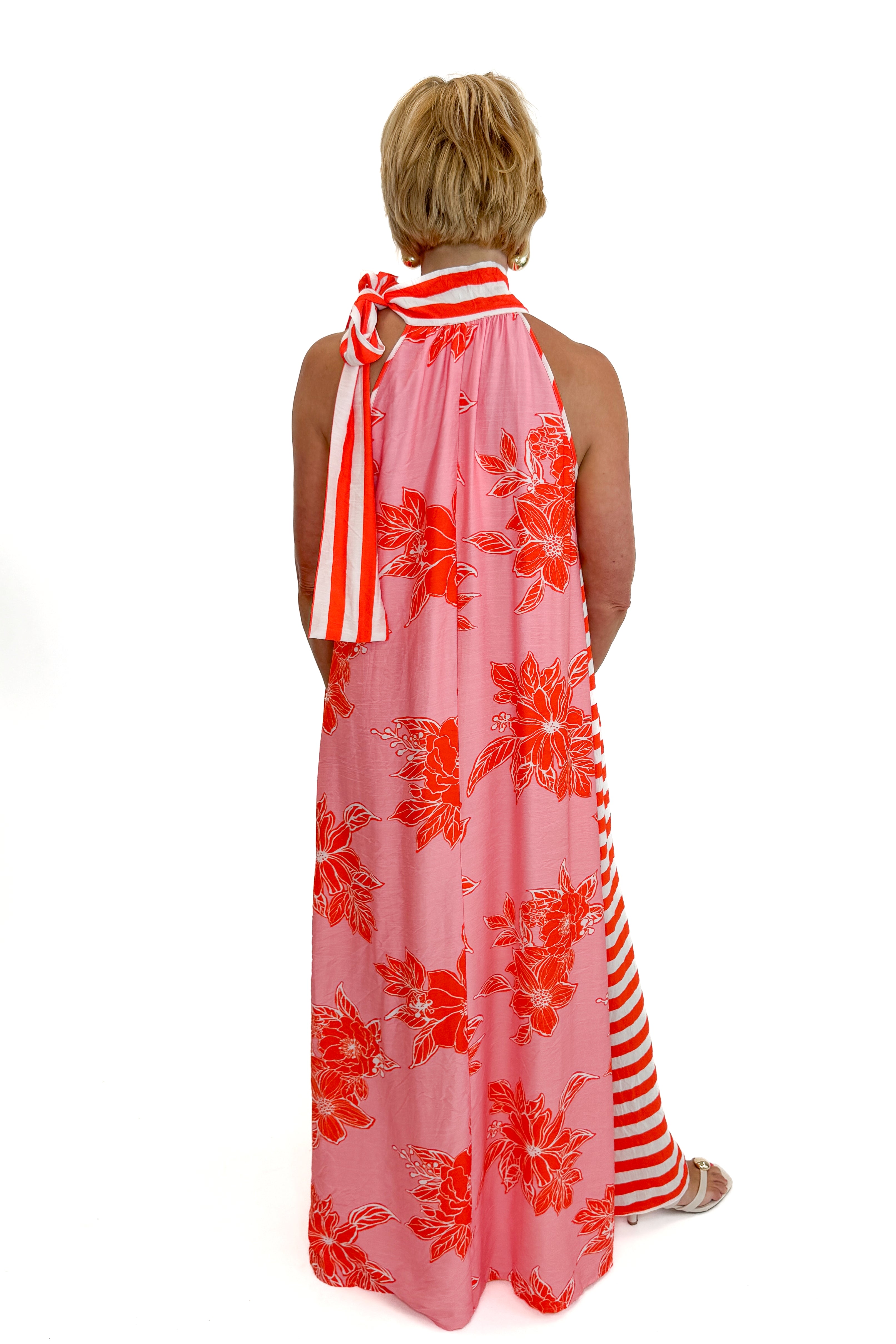 Back view of woman wearing Swagger Boutique’s Pink &amp; Orange Floral &amp; Stripe Maxi Dress by Entro with heels against white studio background.