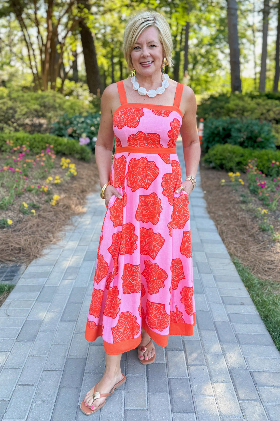 Front view of woman wearing Swagger Boutique’s Pink &amp; Orange Printed Midi Dress by Entro with sandals walking outside down a path.