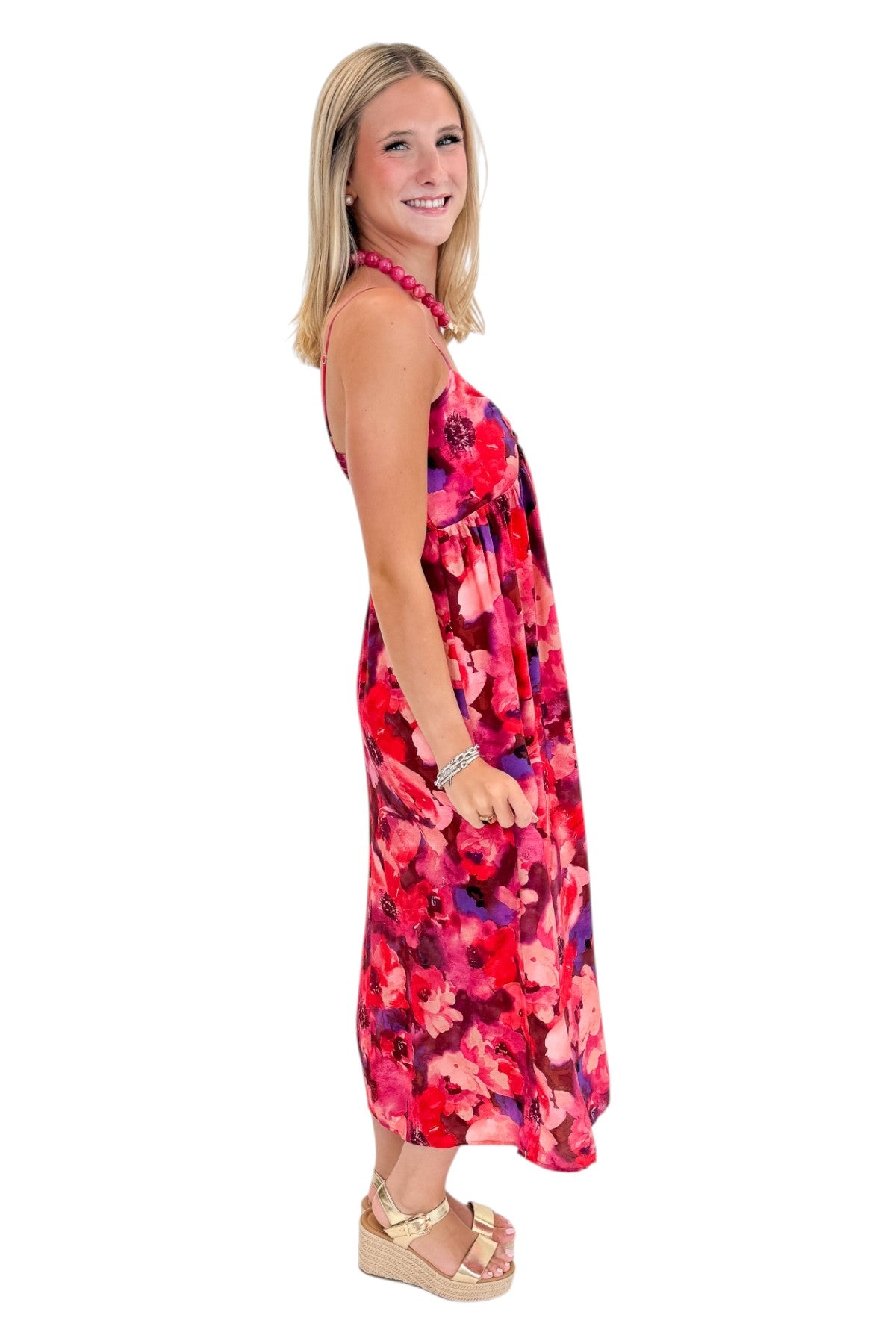 Side view of woman wearing Swagger Boutique’s Pink &amp; Red Floral Midi Dress with sandals against white studio background.