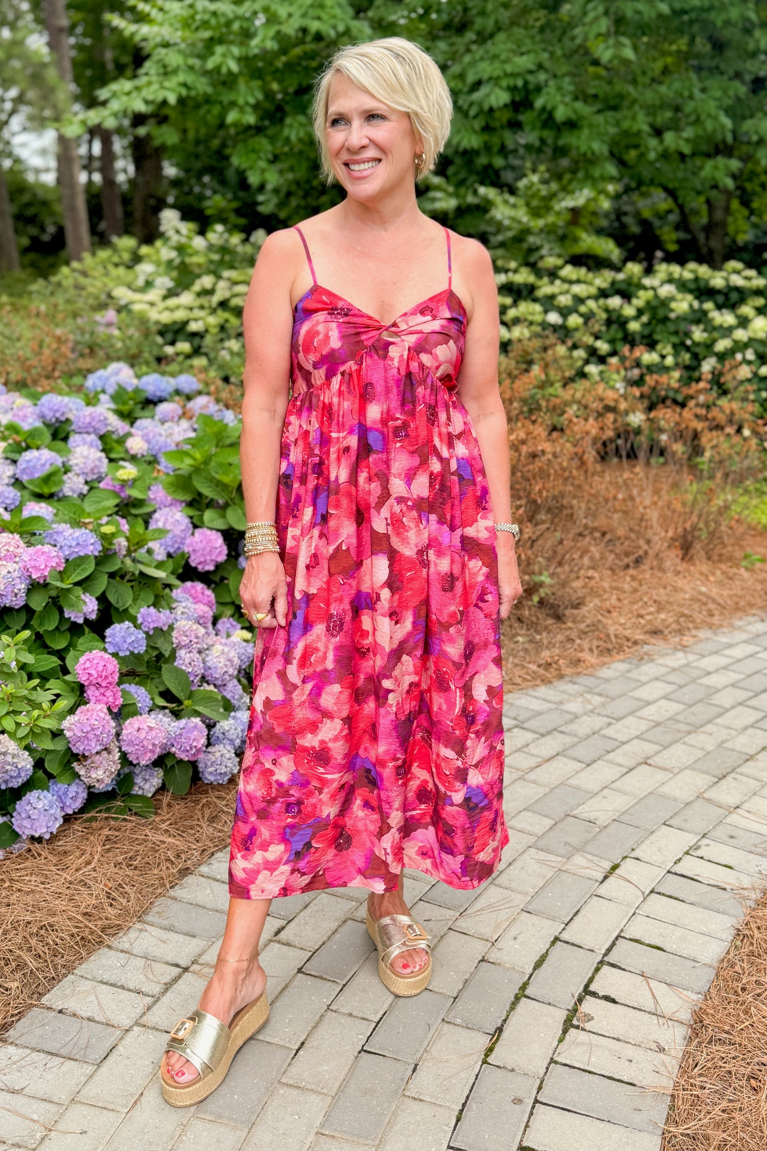 Front view of woman wearing Swagger Boutique’s Pink &amp; Red Floral Midi Dress with sandals standing outside on a path.