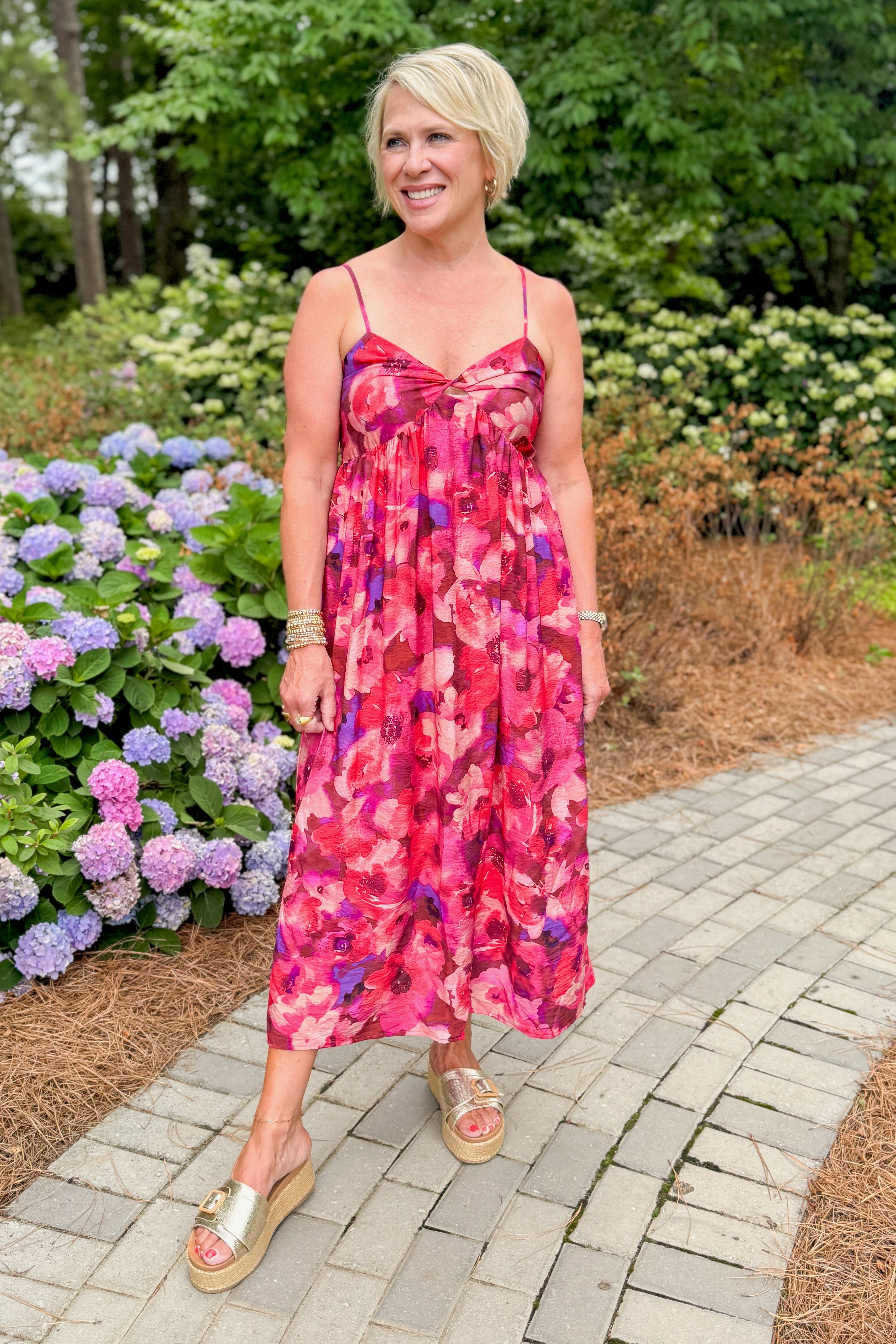 Front view of woman wearing Swagger Boutique’s Pink &amp; Red Floral Midi Dress with sandals standing outside on a path.