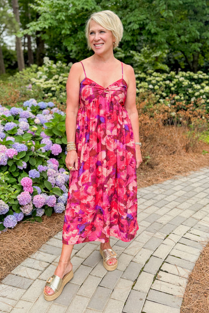 Front view of woman wearing Swagger Boutique’s Pink &amp; Red Floral Midi Dress with sandals standing outside on a path.
