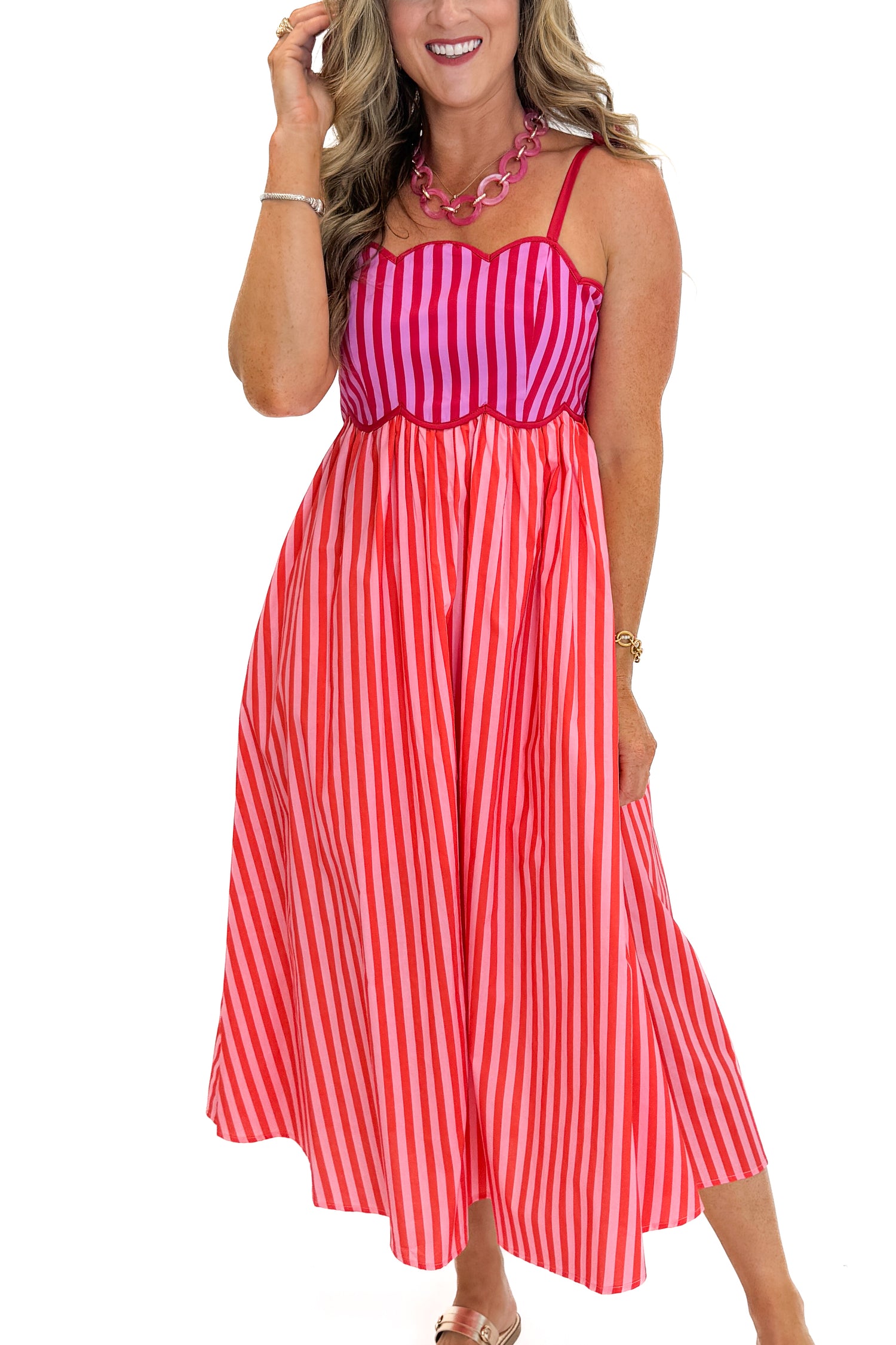Front detail view of woman wearing Swagger Boutique’s Pink &amp; Red Striped Scalloped Midi Dress by Entro with sandals against white studio background.