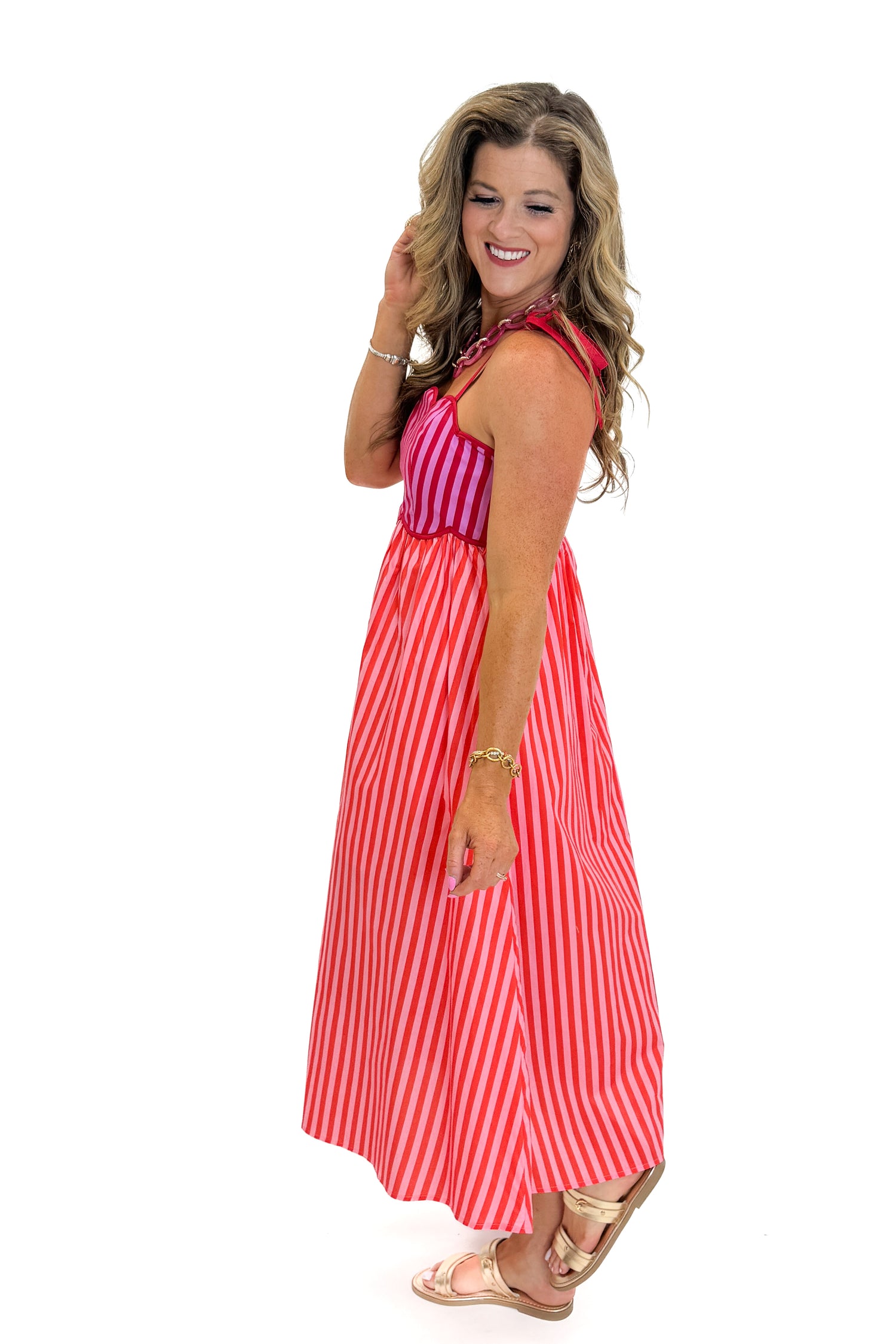 Side view of woman wearing Swagger Boutique’s Pink &amp; Red Striped Scalloped Midi Dress by Entro with sandals against white studio background.