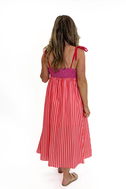 Back view of woman wearing Swagger Boutique’s Pink &amp; Red Striped Scalloped Midi Dress by Entro with sandals against white studio background.