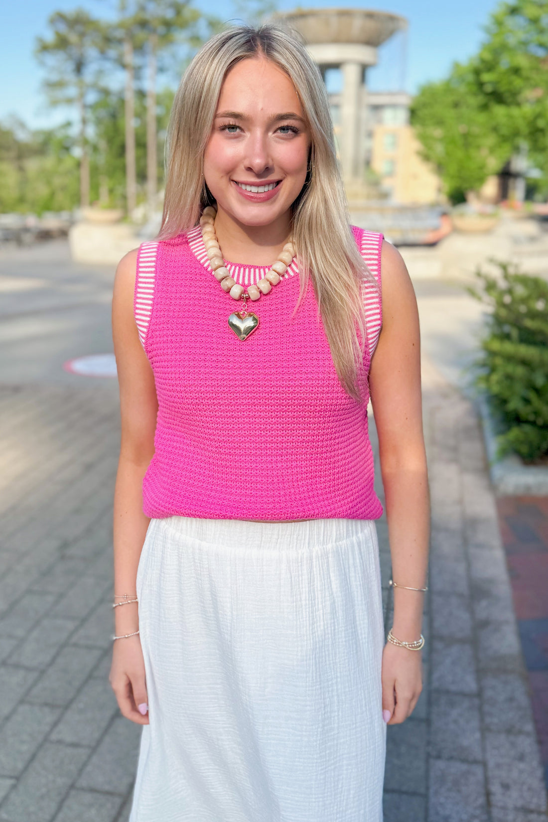 Front view of woman wearing Above All Else Pink &amp; White Textured Sweater Tank with white skirt walking outside.