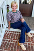 Front view of woman wearing Swagger Boutique’s Plum Jacquard Bubble Sleeve Top with jeans sitting on a front porch step.