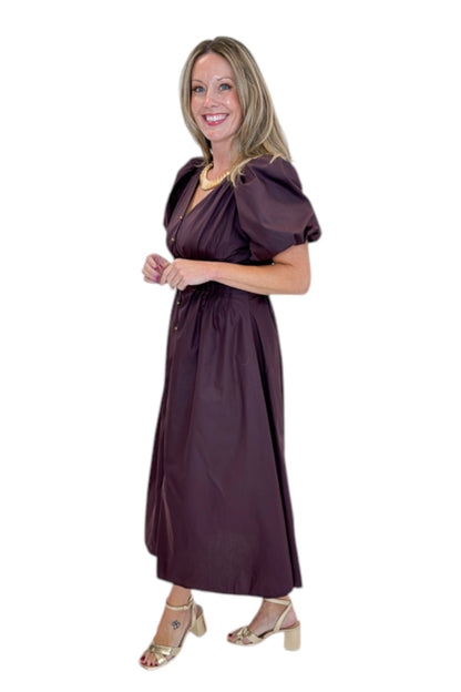 Side view of woman wearing Swagger Boutique’s Plum Pleated Waist Midi Dress by Entro with heels against white studio background.