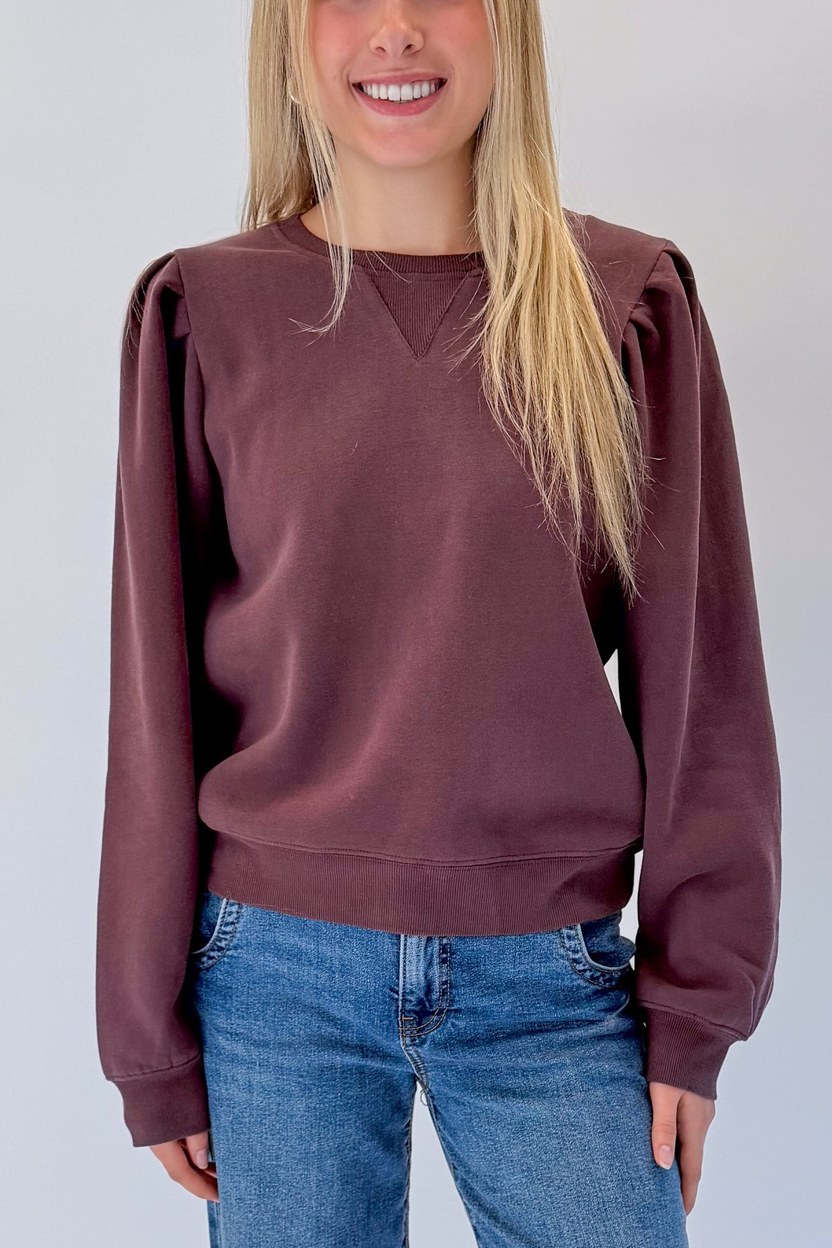 Front detail view of woman wearing Swagger Boutique’s Plum Puff Sleeve Sweatshirt with jeans against white studio background.