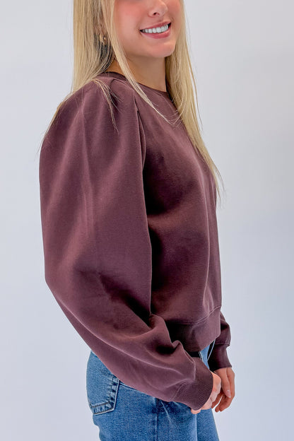 Side detail view of woman wearing Swagger Boutique’s Plum Puff Sleeve Sweatshirt with jeans against white studio background.
