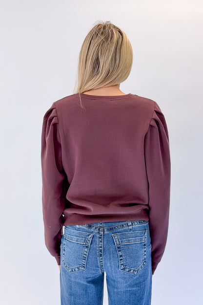 Back view of woman wearing Swagger Boutique’s Plum Puff Sleeve Sweatshirt with jeans against white studio background.