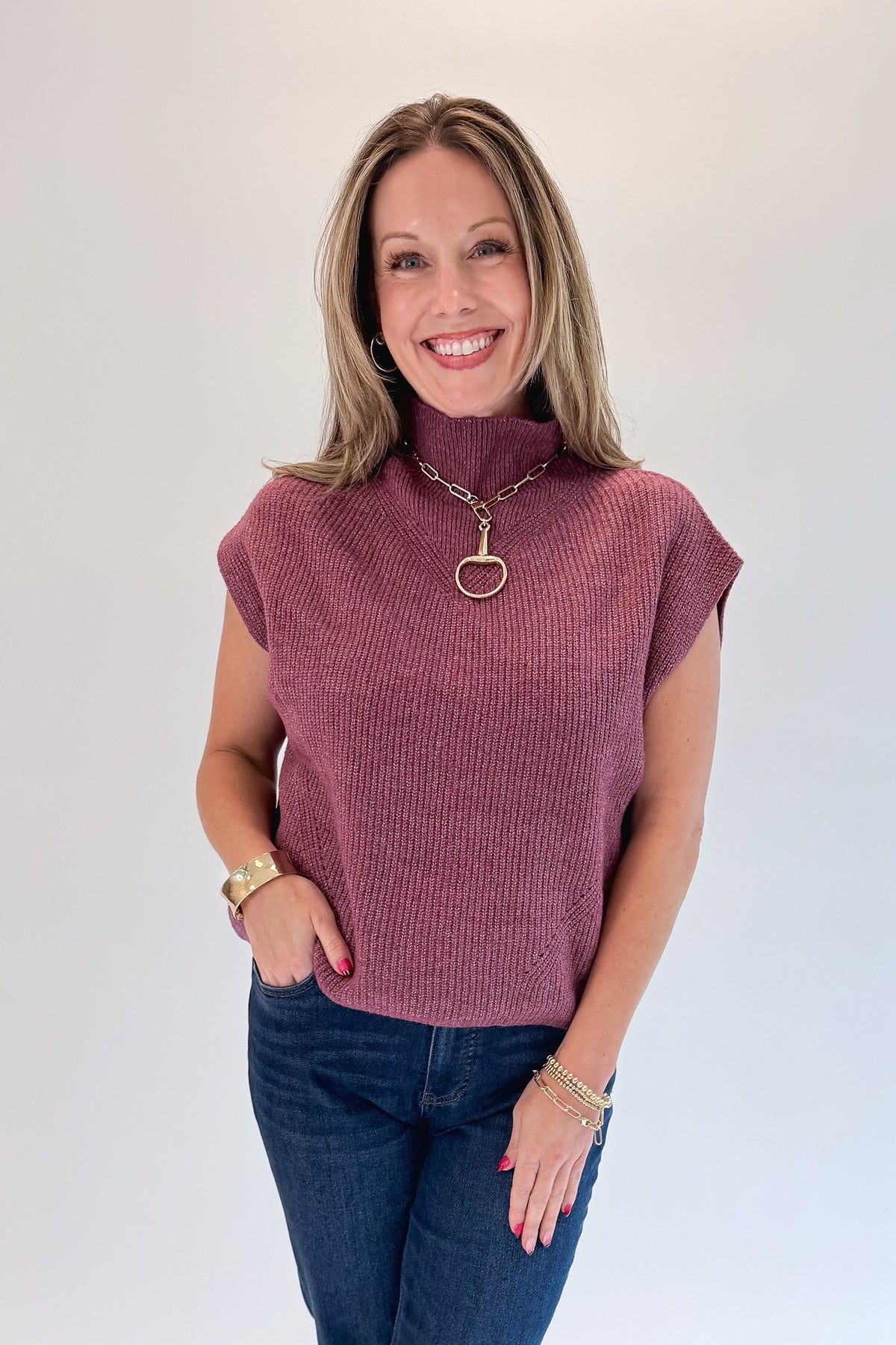 Front view of woman wearing Swagger Boutique’s Plum Sleeveless Mock Neck Sweater with jeans against white studio background.