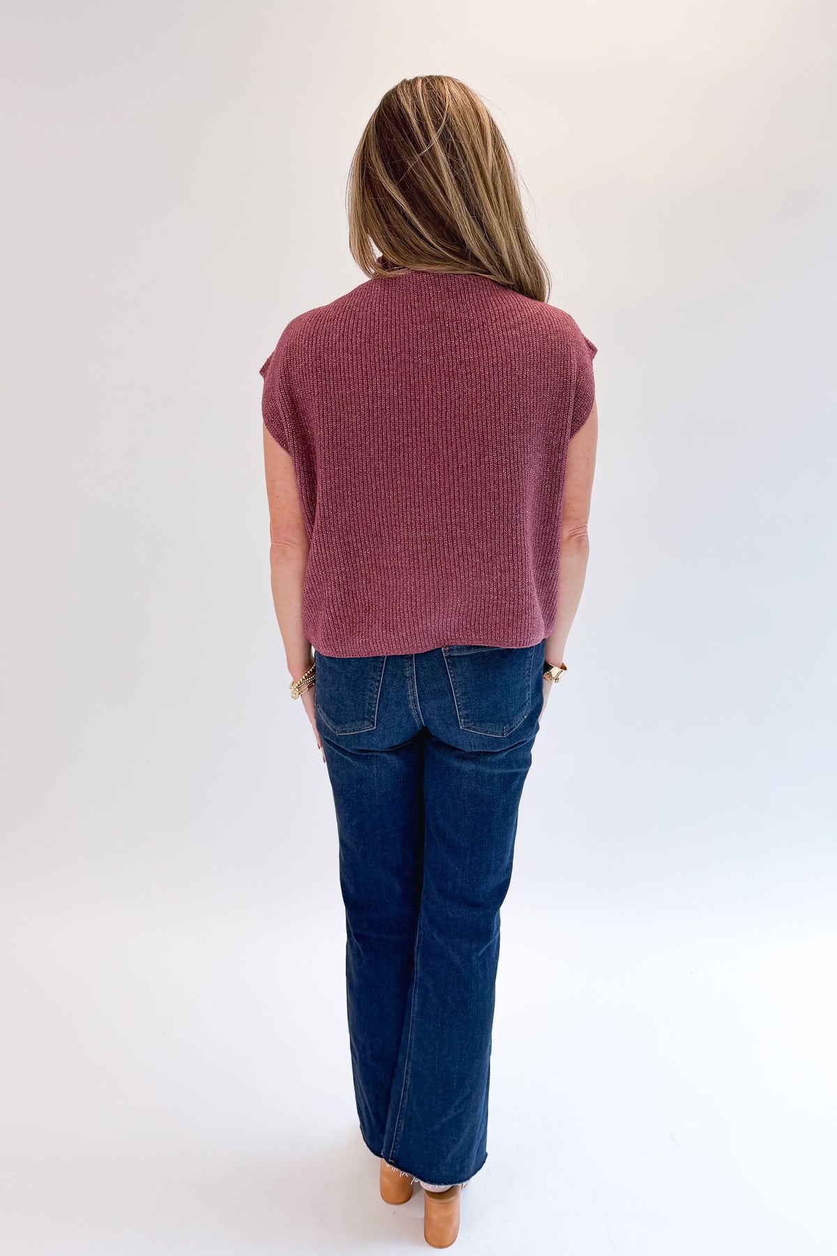 Back view of woman wearing Swagger Boutique’s Plum Sleeveless Mock Neck Sweater with jeans against white studio background.