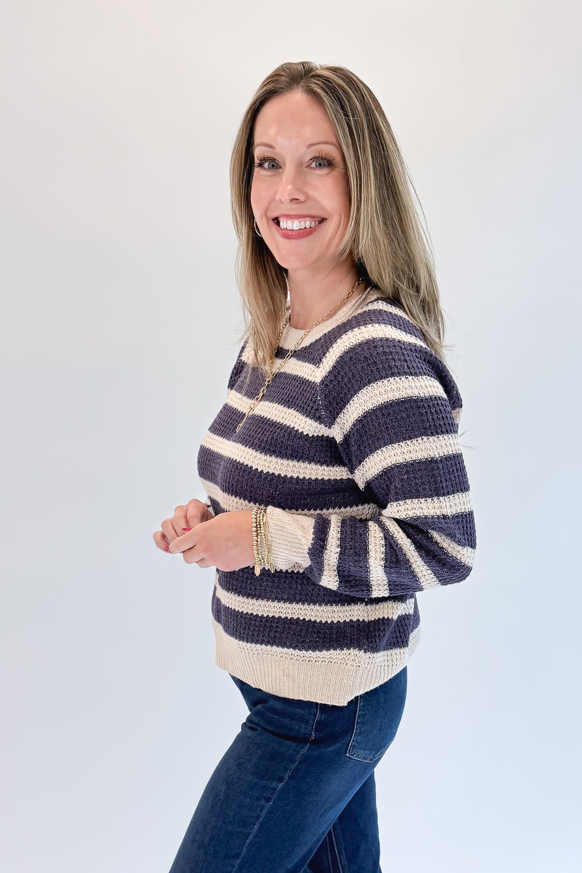 Side view of woman wearing Swagger Boutique’s Plum Striped Waffle Weave Sweater with jeans against white studio background.